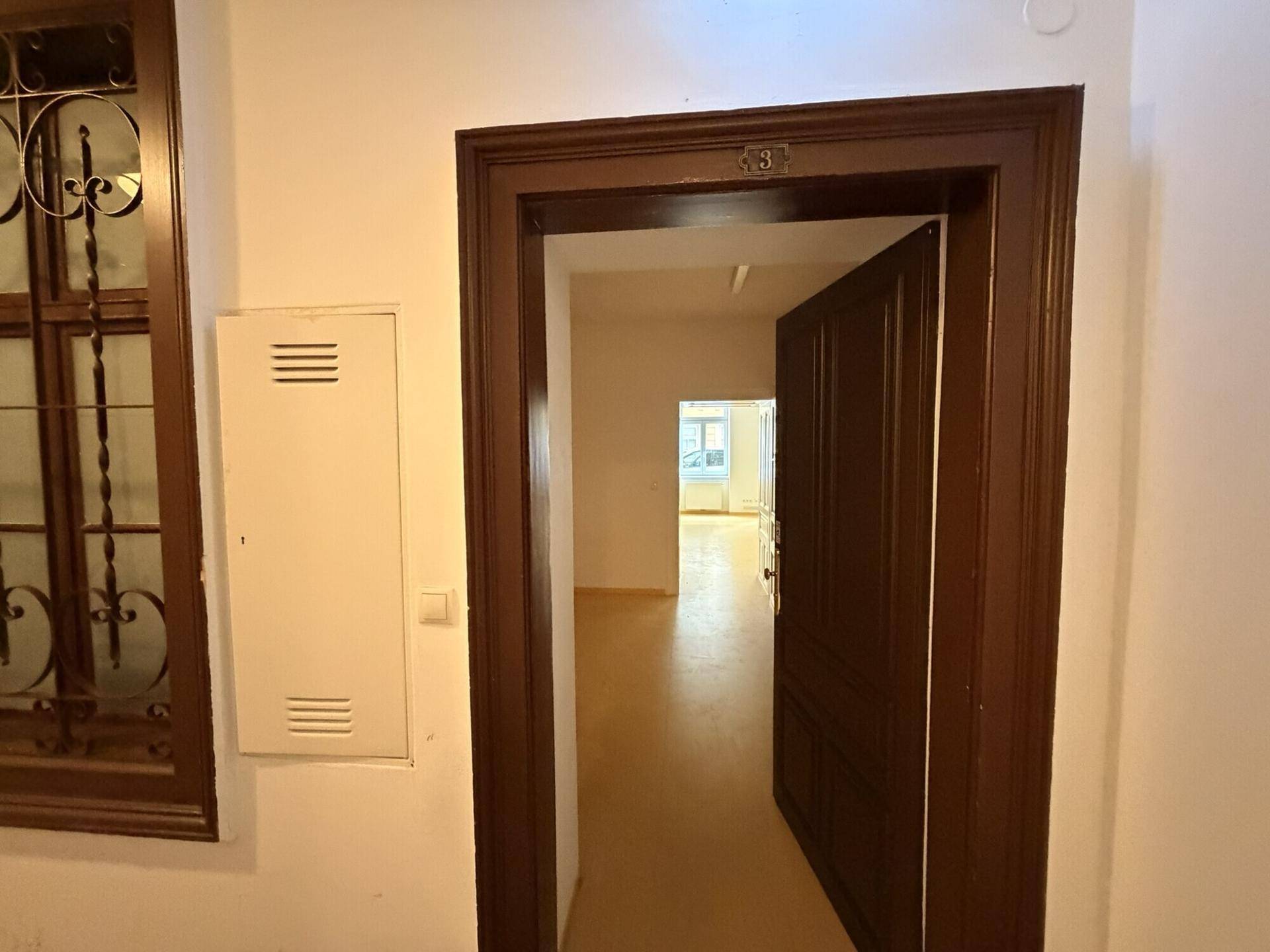 Blick durch eine offene Holztür in einen weiteren Raum, mit einem dekorativen Fenster im Flurbereich.