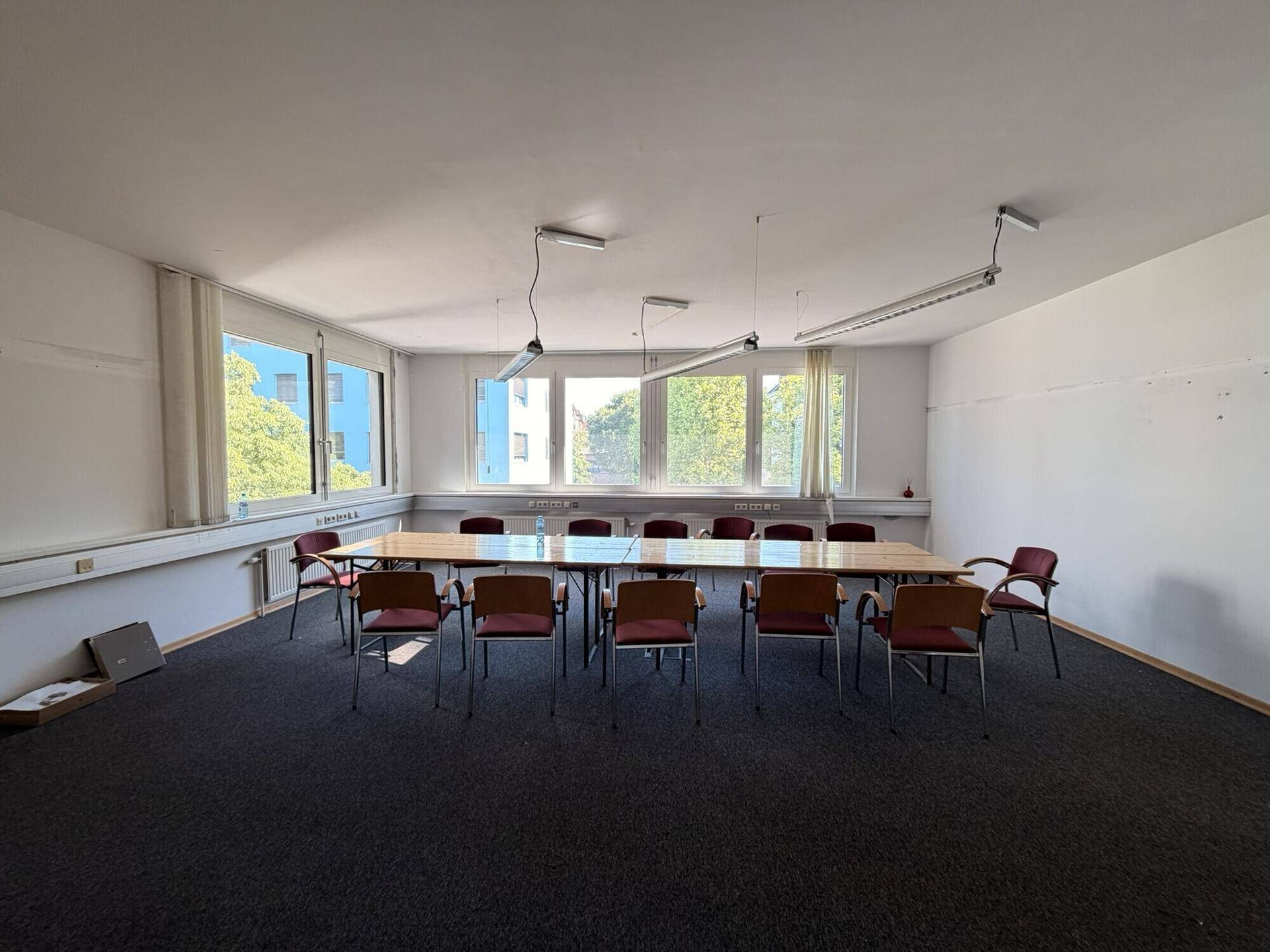 Konferenzraum mit langem Tisch, Stühlen und großen Fenstern, die viel Tageslicht bieten.