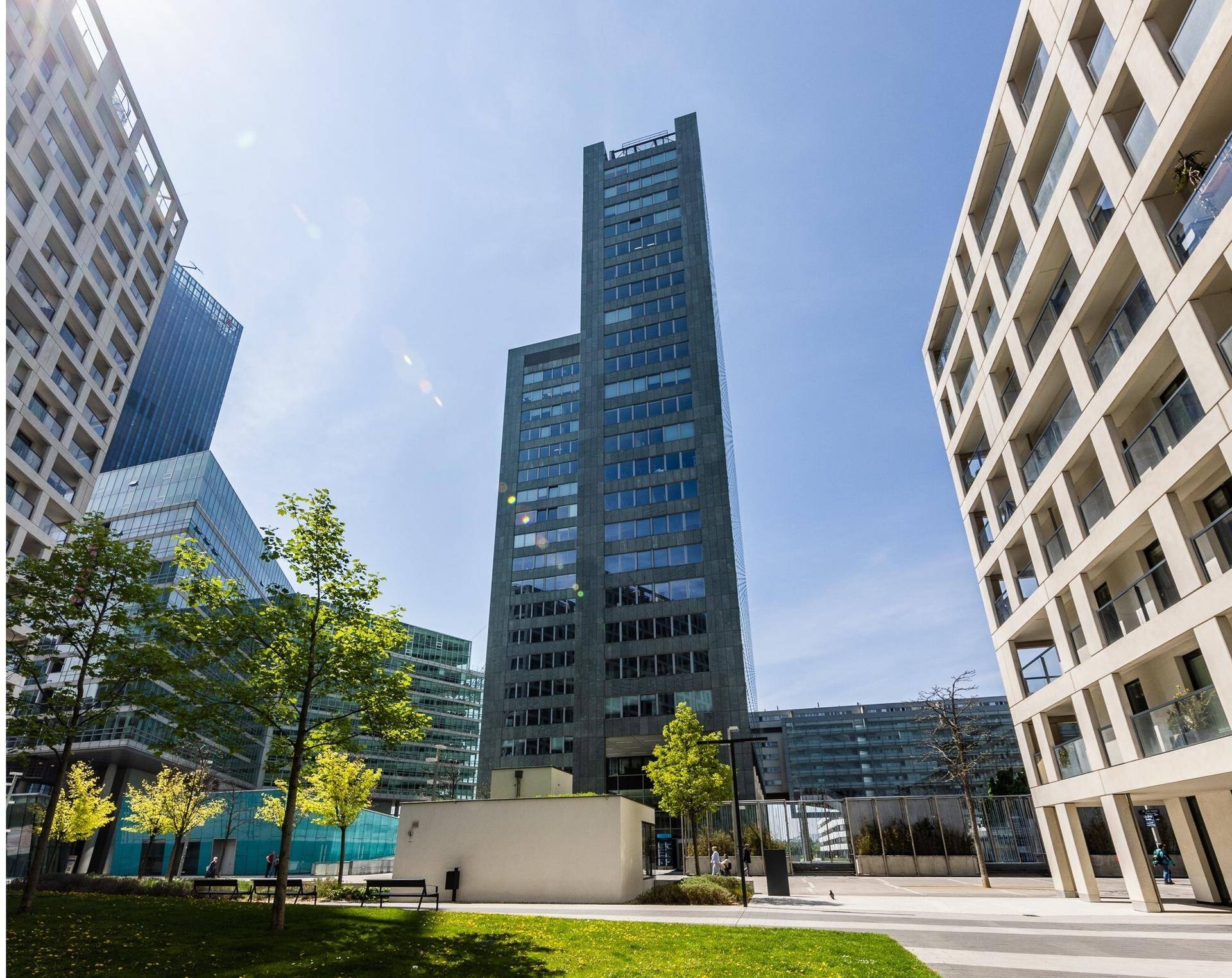 Hohes Bürogebäude in einer modernen Stadtlandschaft mit umliegenden Gebäuden und Grünflächen.