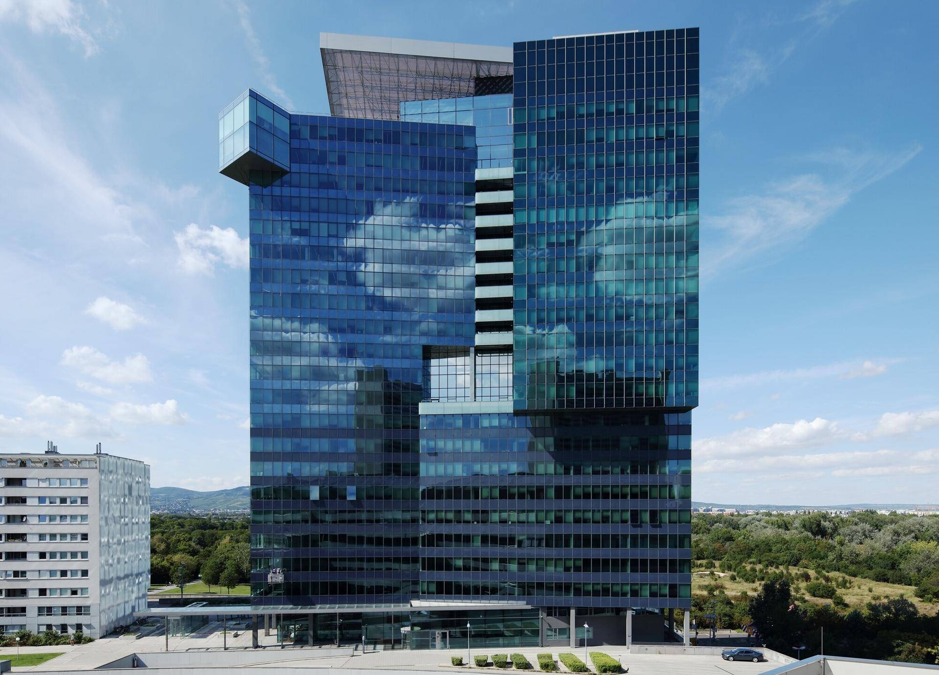 Beeindruckendes modernes Hochhaus mit spiegelnder Glasfassade unter blauem Himmel und grüner Umgebung.