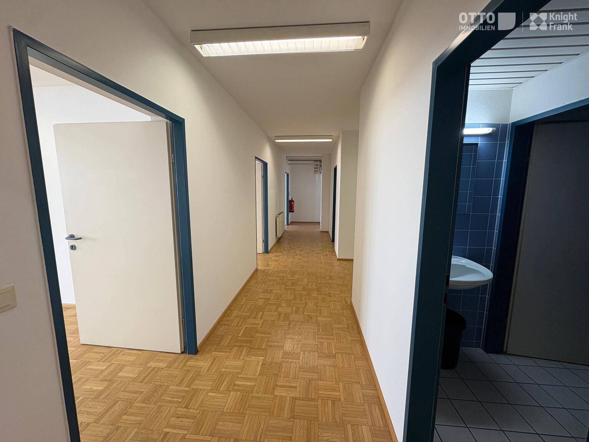Langer Flur mit Parkettboden und mehreren Türen, der verschiedene Büroräume verbindet.