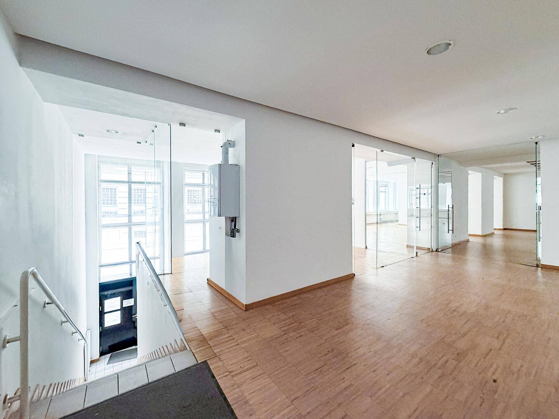Eingangsbereich mit Treppe, Parkettboden und Glastrennwänden, der zu den oberen Büroräumen führt.