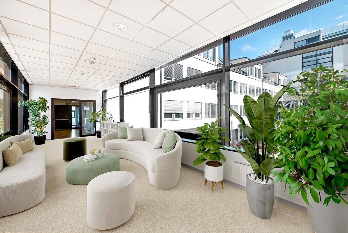 Geräumiger Loungebereich mit bequemen Sofas, vielen Pflanzen und großen Fenstern mit Stadtblick.