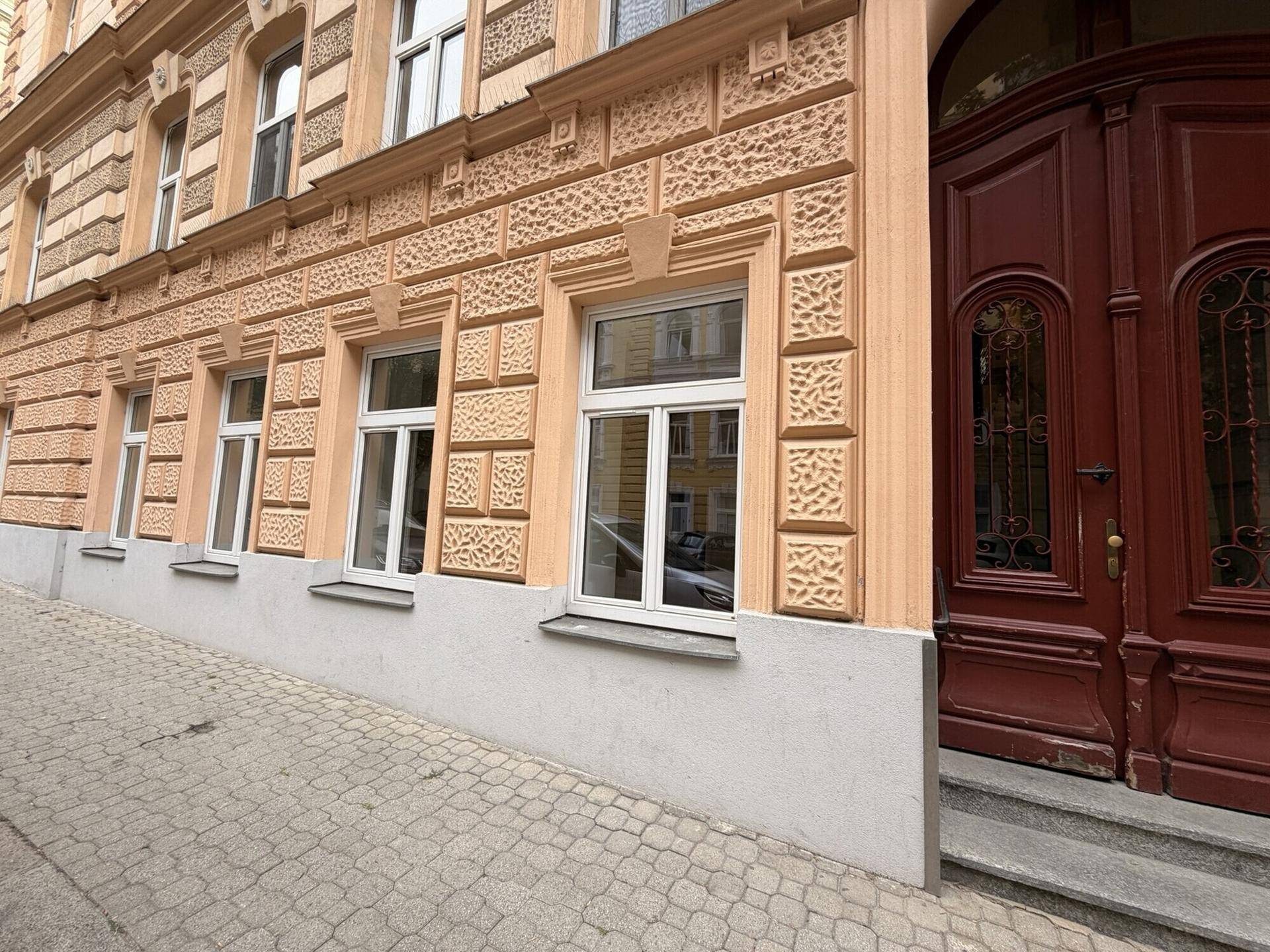 Nahaufnahme der Fassade mit weißen Fenstern und einer großen, verzierten Holztür des Gebäudes.