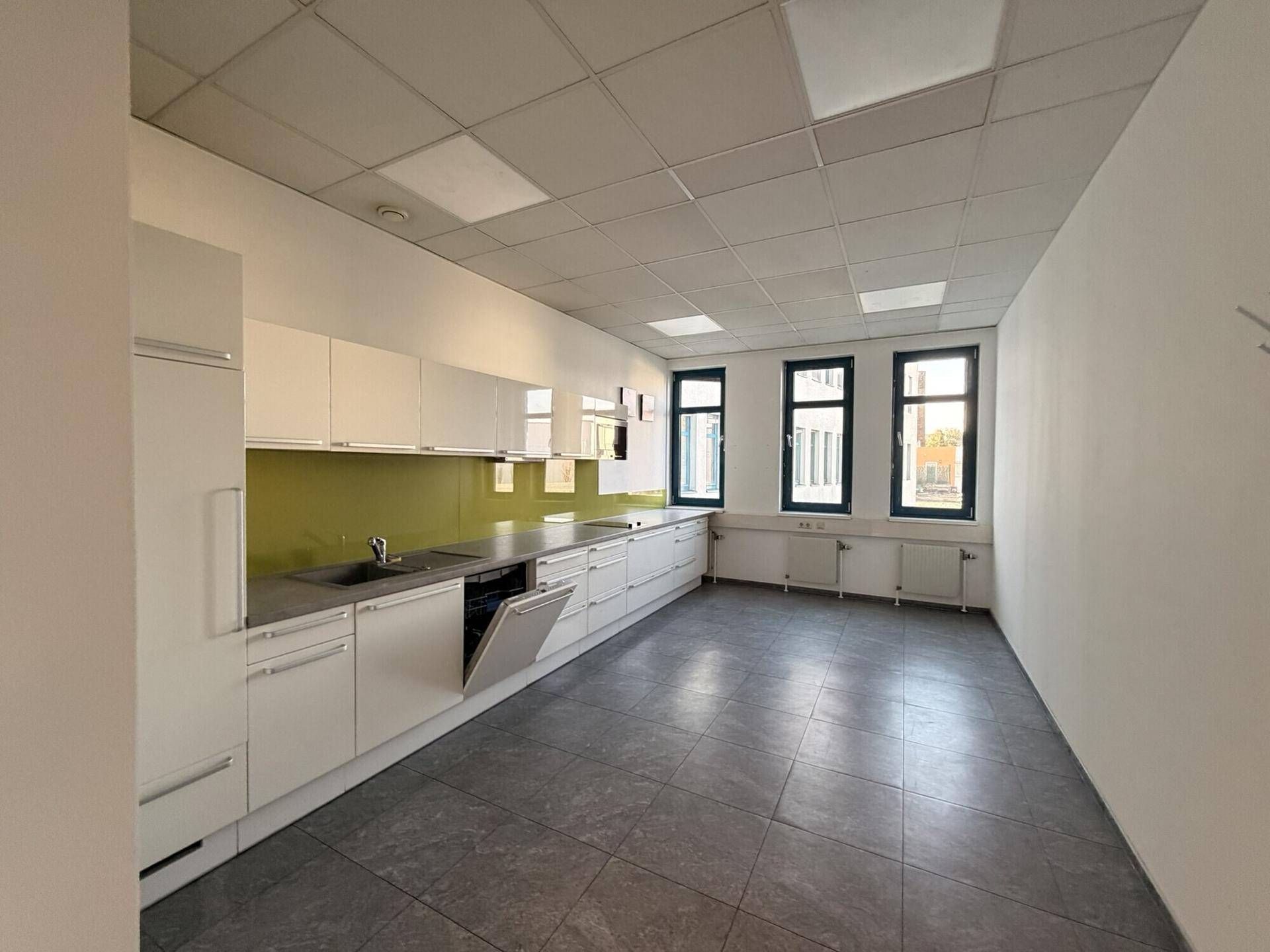 Moderne Einbauküche in einem Büro mit weißen Schränken, Spülmaschine und Fliesenboden.