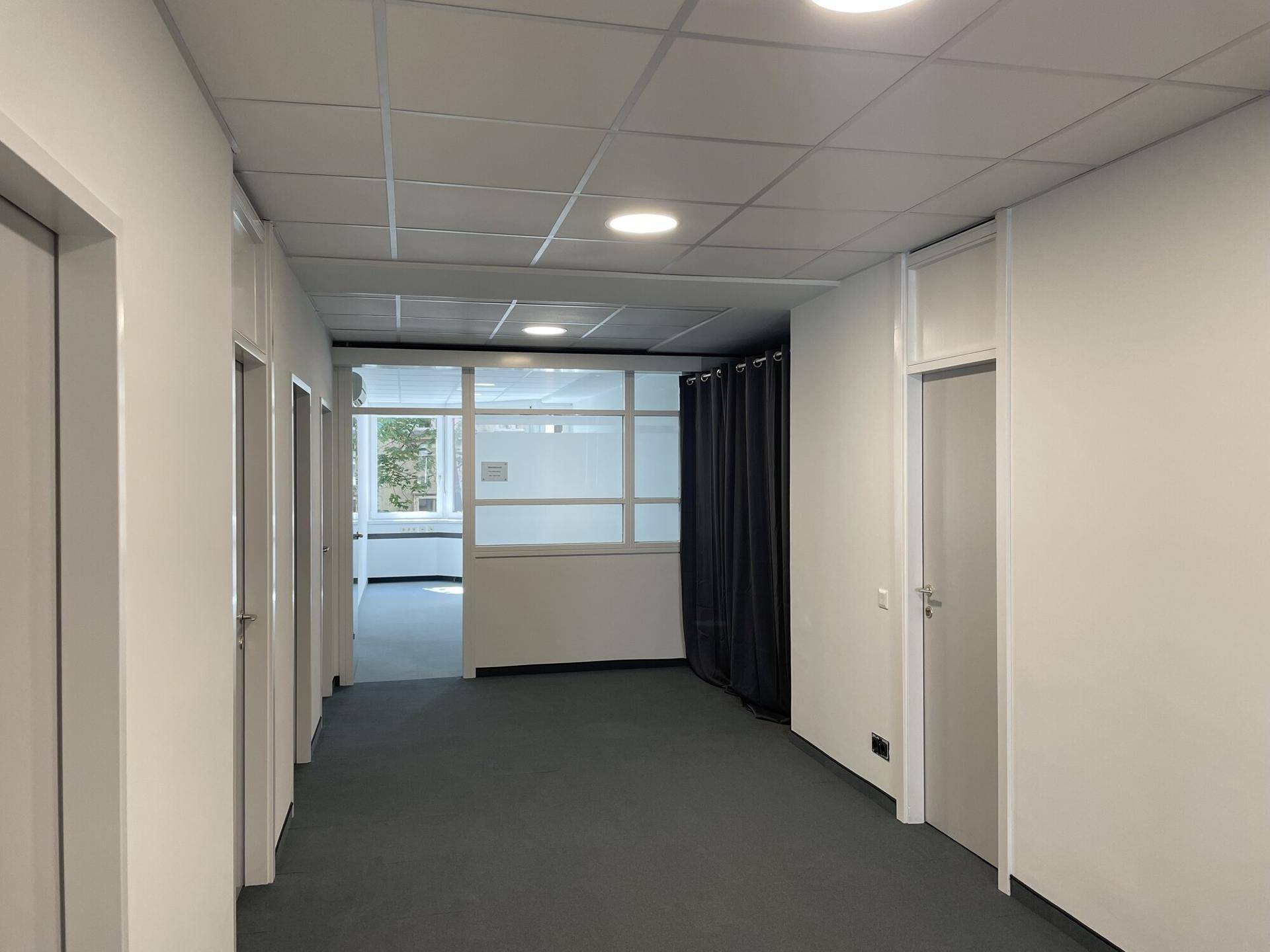 Langer Flur mit Teppichboden, mehreren Türen und einem Blick in einen weiteren Bürobereich.