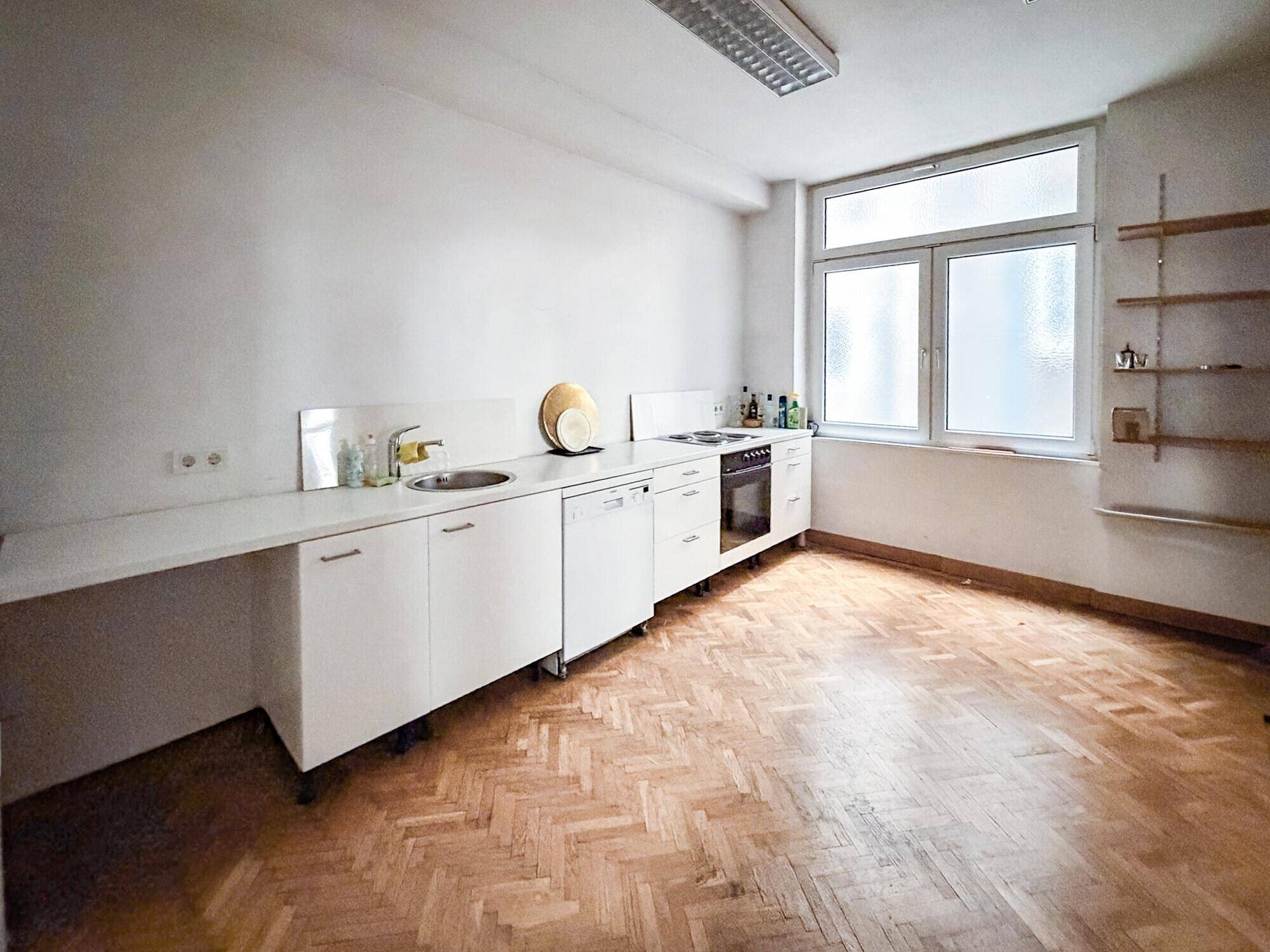 Einfache Küche mit weißen Unterschränken, Spüle, Herd und einem Fenster für natürliches Licht.