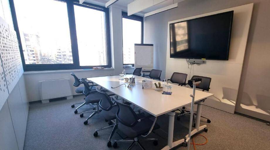 Heller Konferenzraum mit großem Tisch, Wandbildschirm und großen Fenstern mit Blick auf die Stadtlandschaft.
