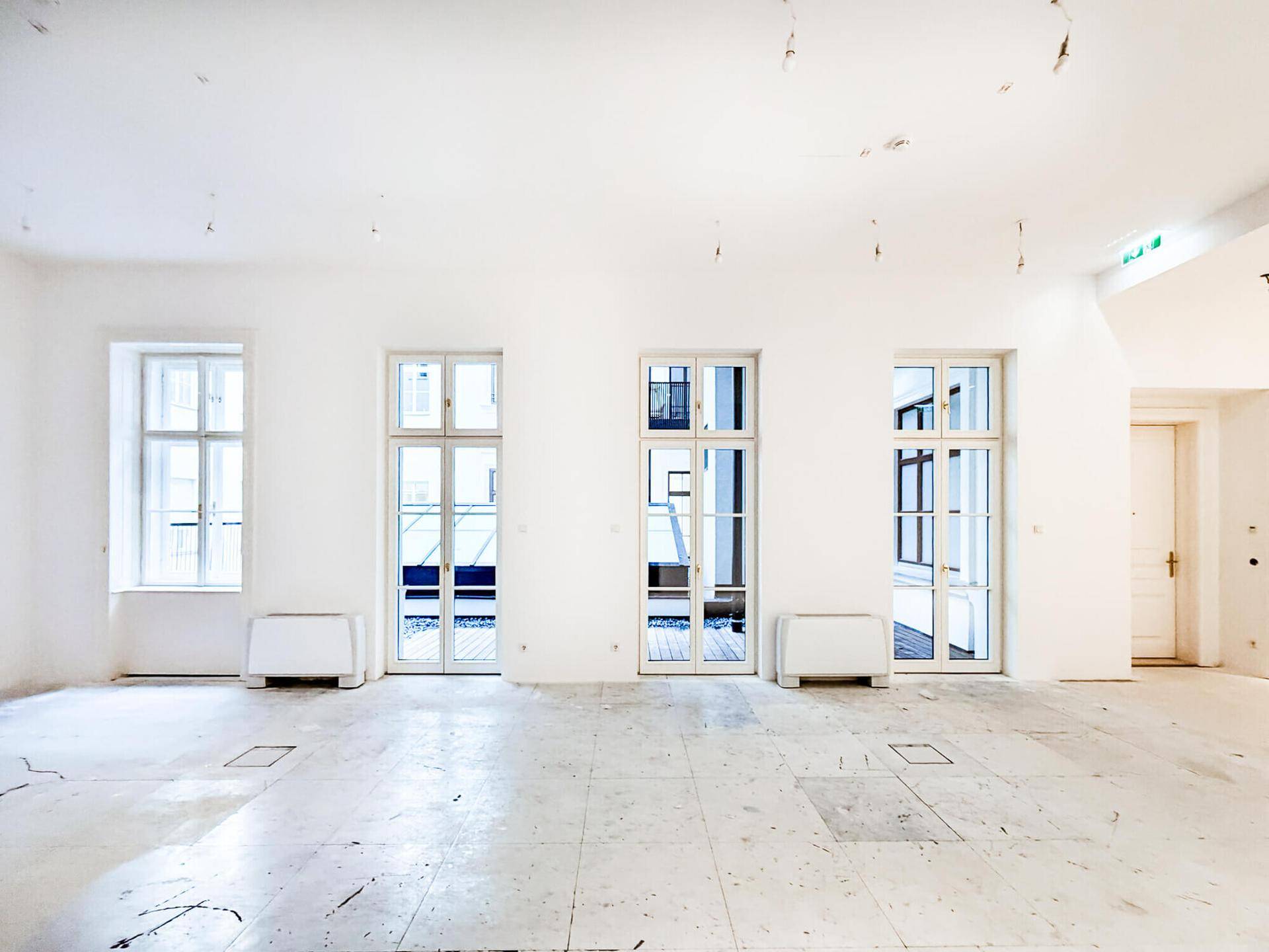 Langer, heller Raum mit mehreren Fenstertüren, die zu einem Außenbereich führen und viel Licht hereinlassen.