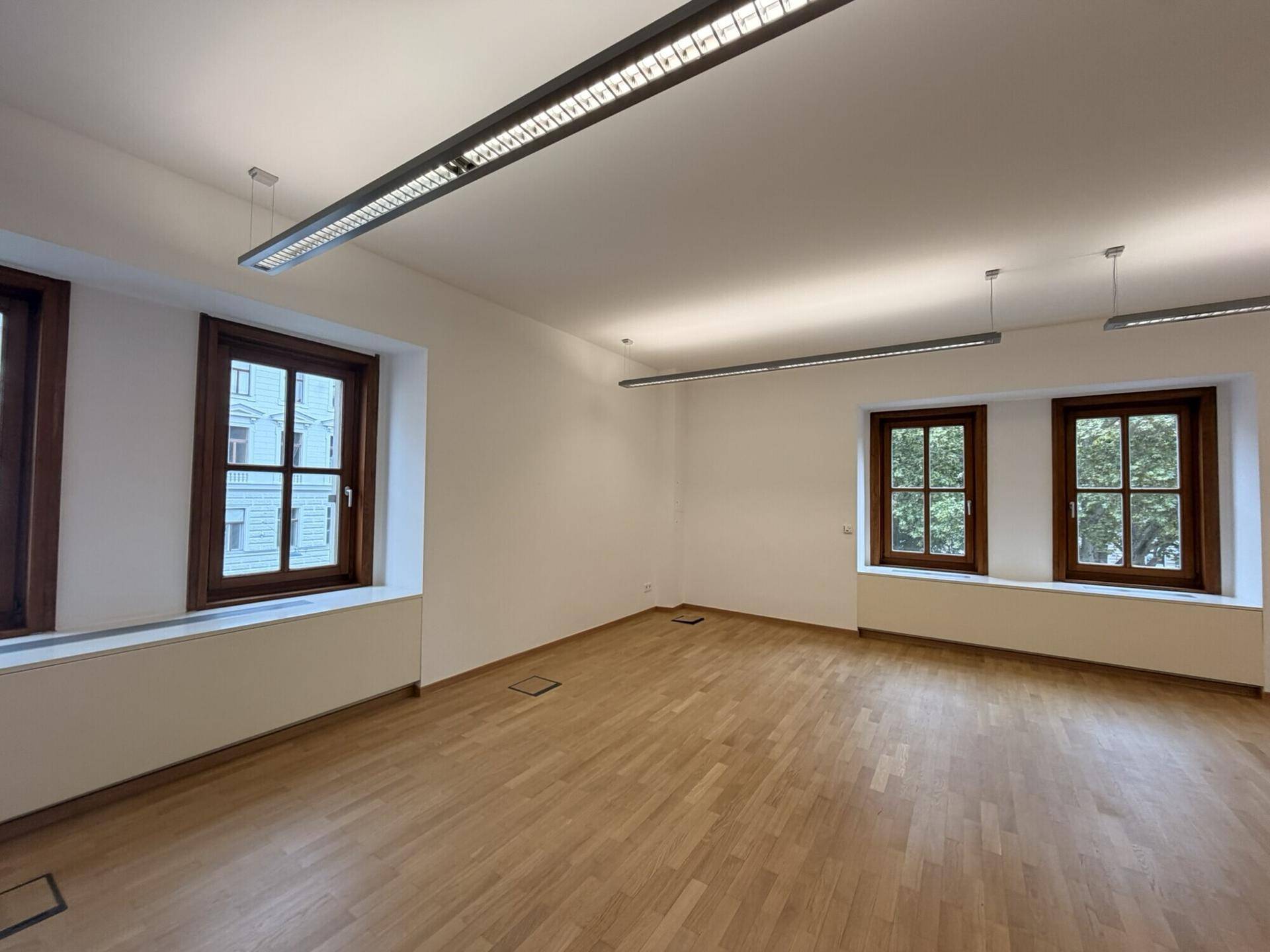 Helles und geräumiges Büro mit Holzparkett und mehreren Fenstern, die eine angenehme Arbeitsatmosphäre schaffen.