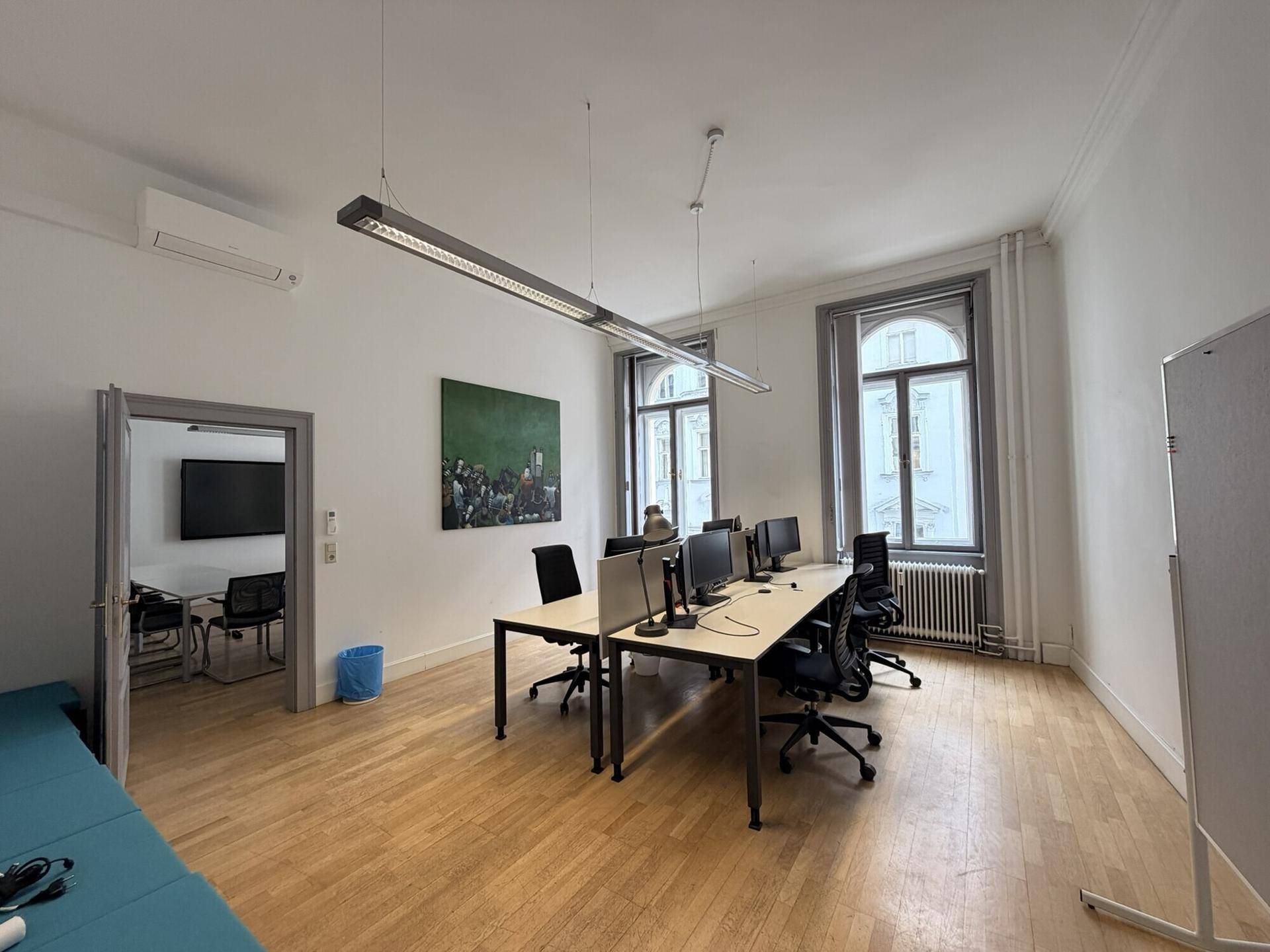 Helles Büro mit mehreren Arbeitsplätzen, Holzboden und großen Fenstern mit Blick nach draußen.