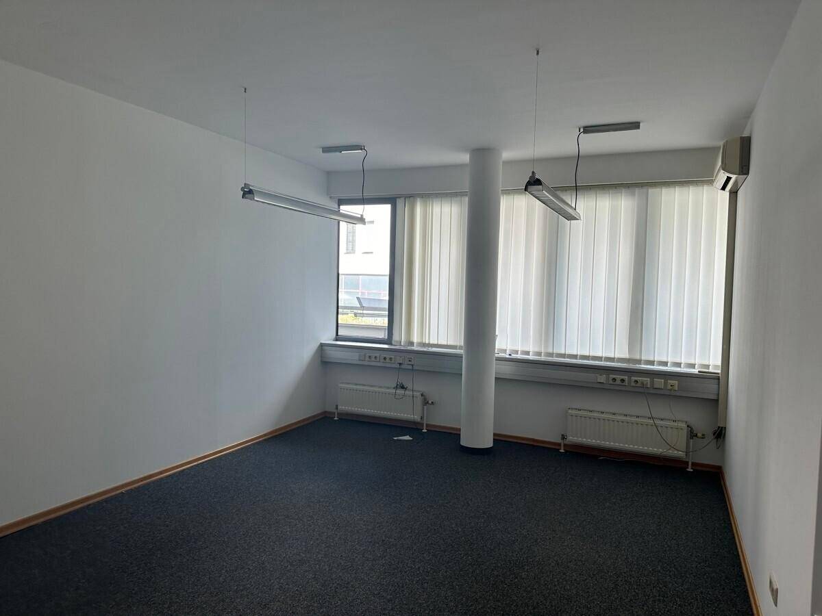Leeres Büro mit Teppichboden, Säule, Fenstern mit Jalousien und einer Klimaanlage.