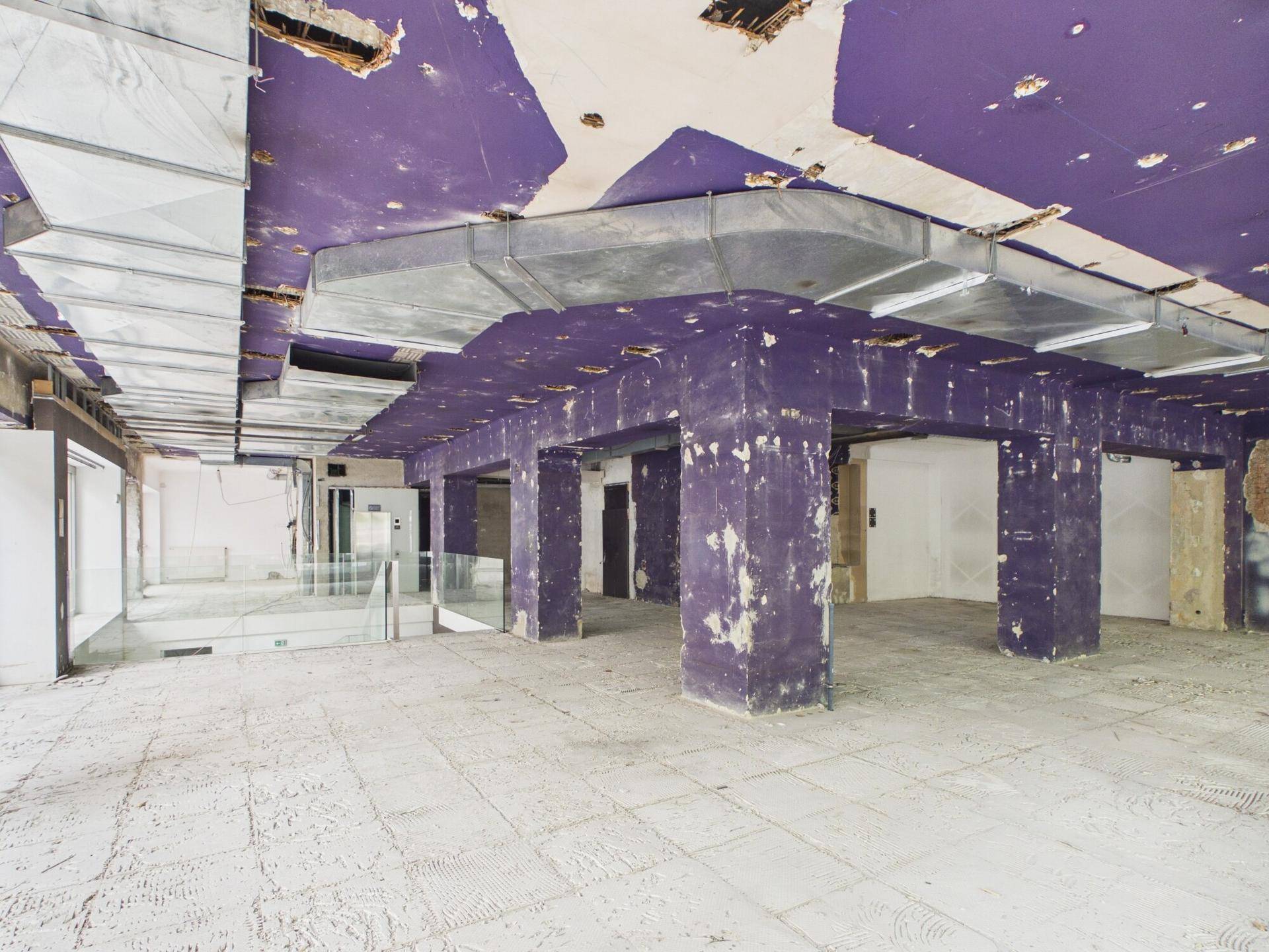 Großer Gewerberaum im Rohzustand mit lila Decke, sichtbaren Lüftungskanälen und Betonboden.