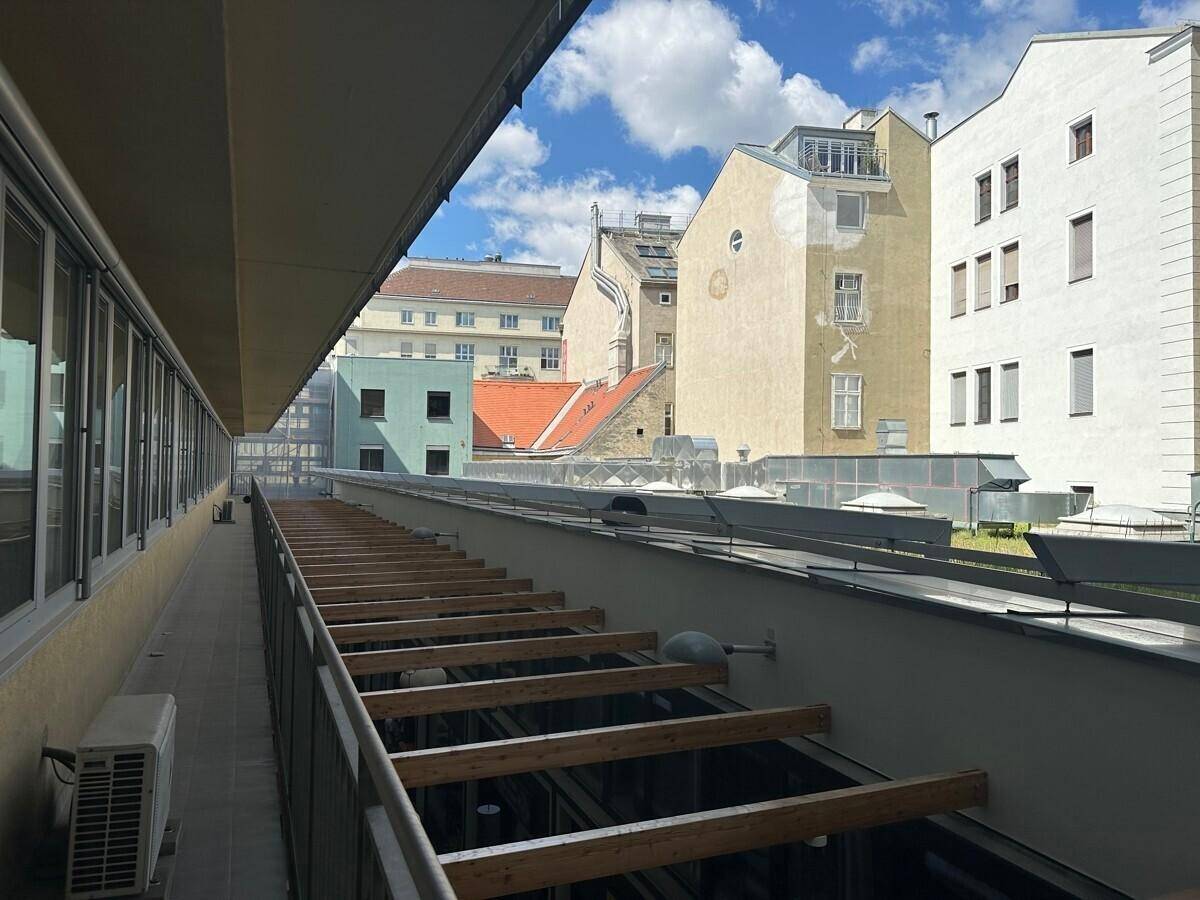Blick von einem Balkon auf die Dächer umliegender Gebäude unter blauem Himmel mit Wolken.