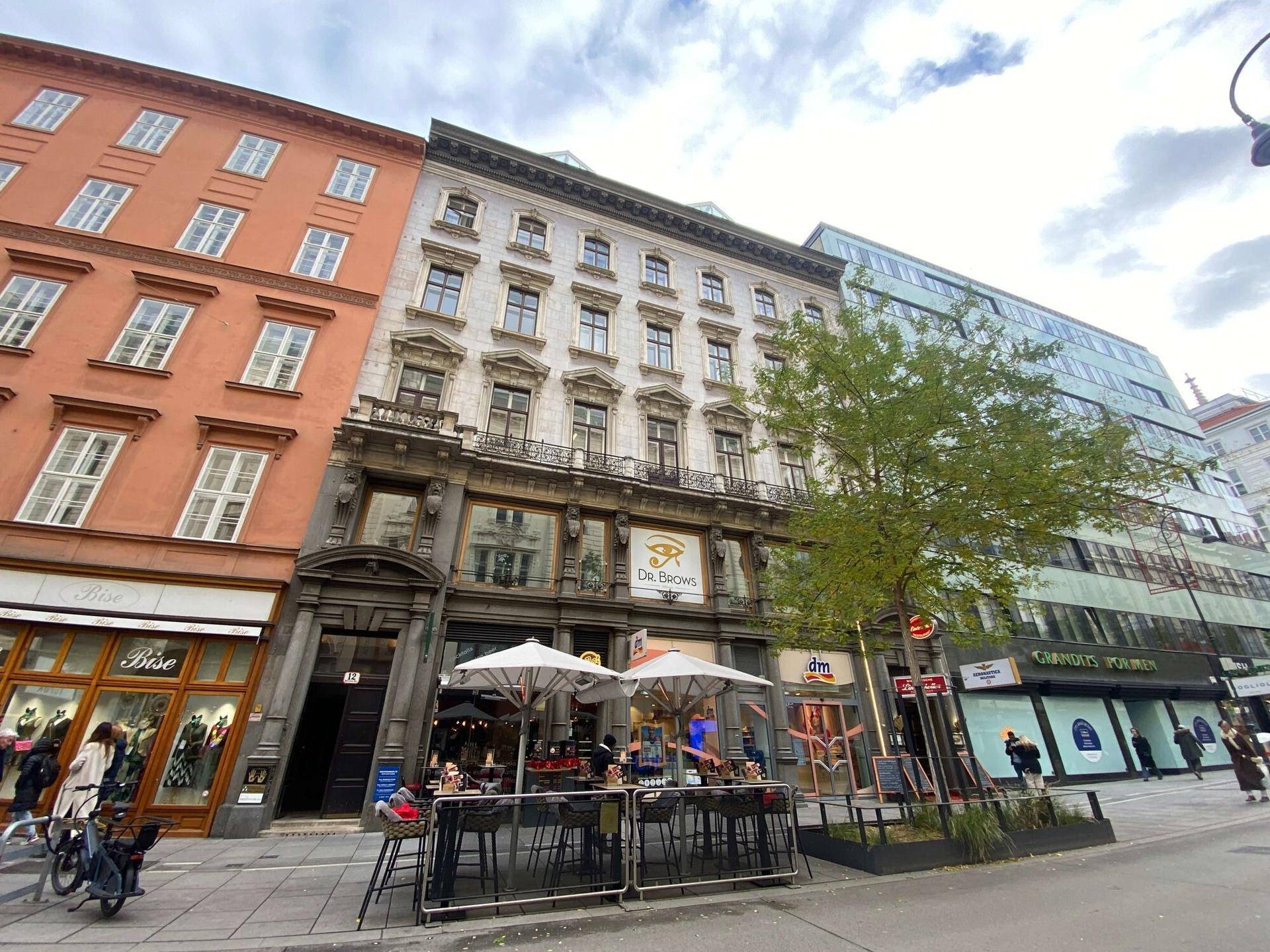 Historische Fassade eines Gebäudes mit Geschäften und Restaurants in einer belebten Stadtstraße.