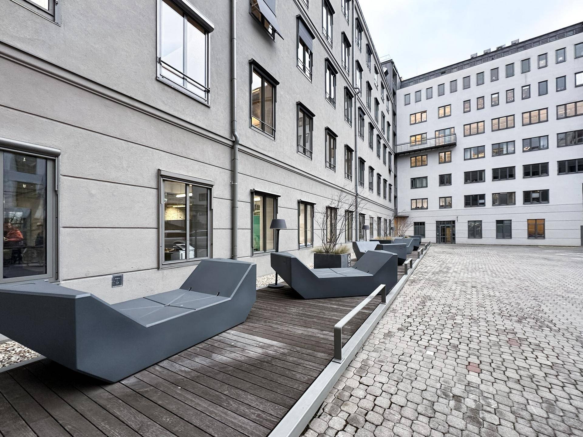 Innenhof mit modernen Sitzgelegenheiten auf Holzdecking, umgeben von Gebäudefassaden, ideal zum Entspannen.