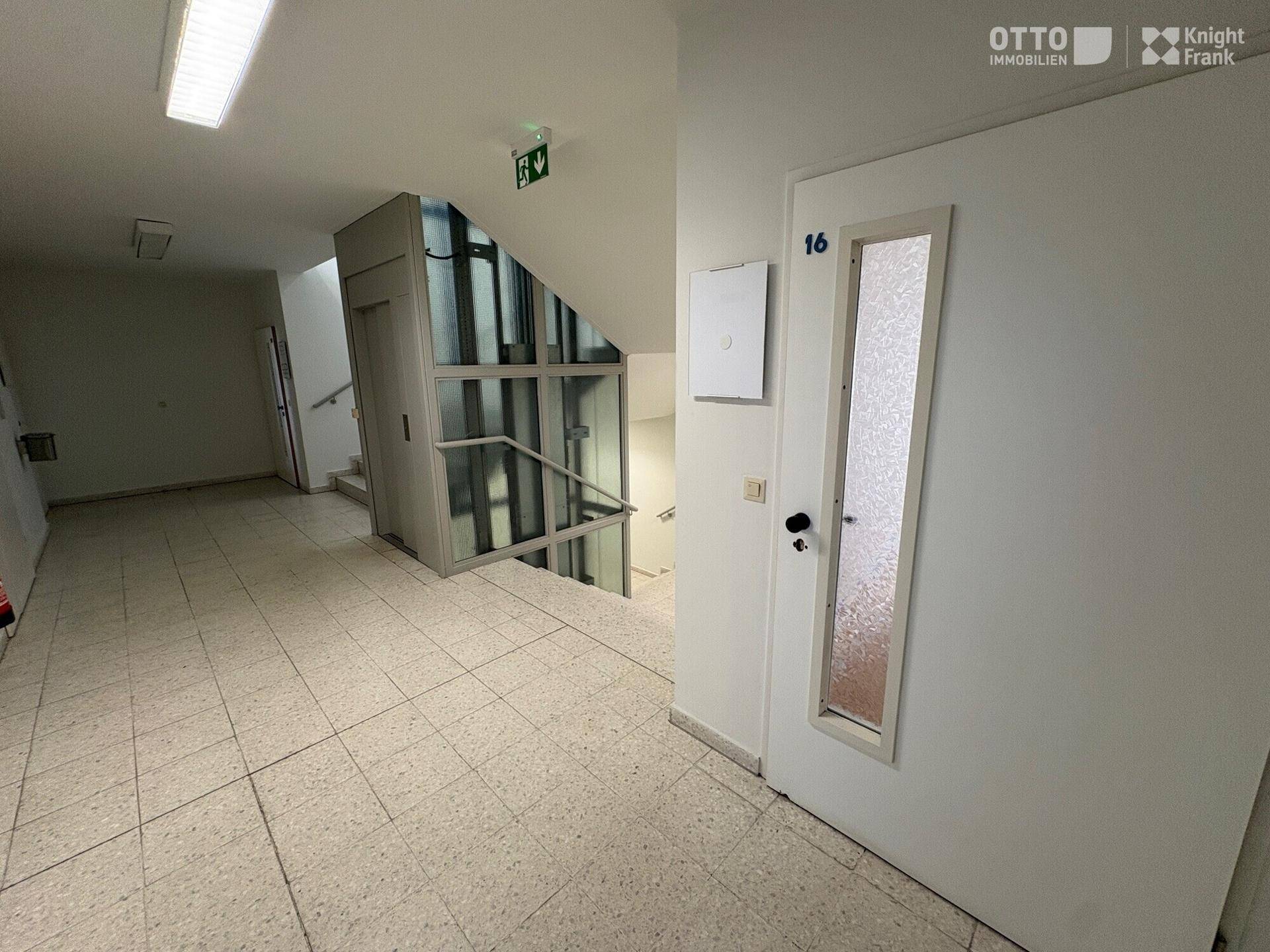 Eingangsbereich mit Treppenhaus und modernem Glasaufzug, der alle Etagen erschließt.