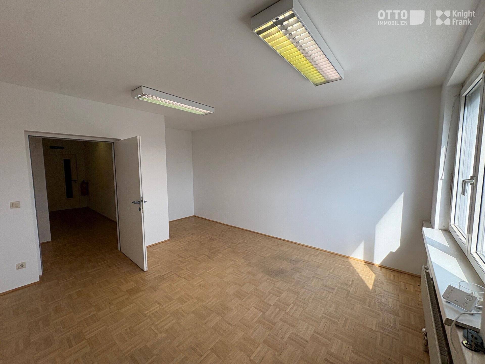 Helles Büro mit Parkettboden und Fensterfront, die viel natürliches Licht hereinlässt und eine angenehme Arbeitsatmosphäre schafft.
