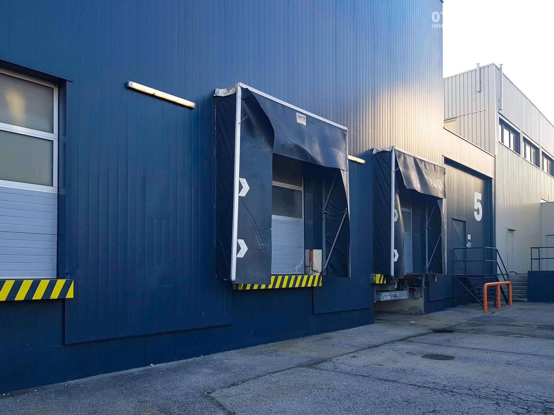 Nahaufnahme der blauen Fassade eines Industriegebäudes mit zwei Laderampen und gelben Sicherheitsmarkierungen.