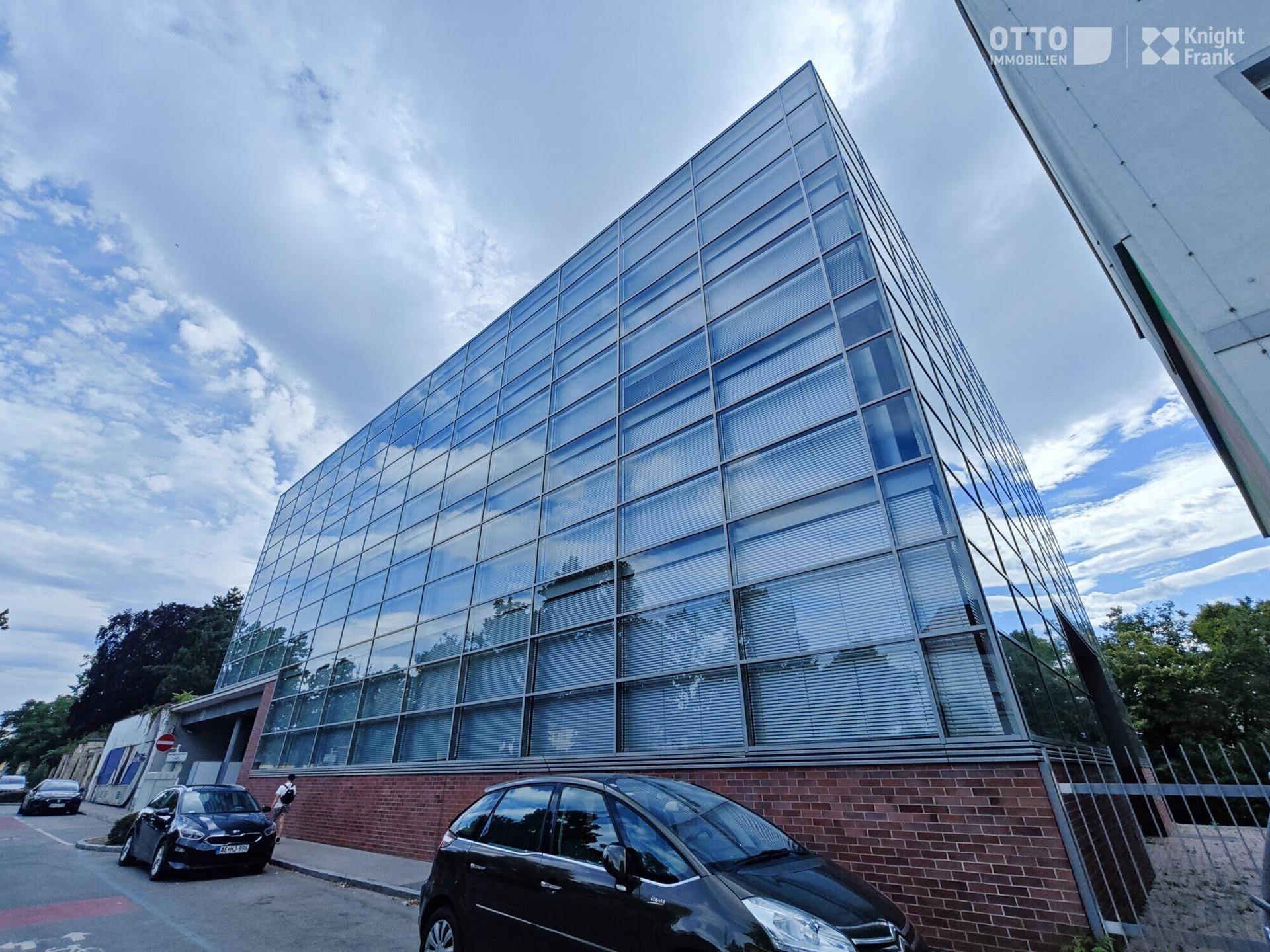 Schräge Ansicht des modernen Gebäudes mit reflektierender Glasfassade und Ziegelunterbau an der Straße.