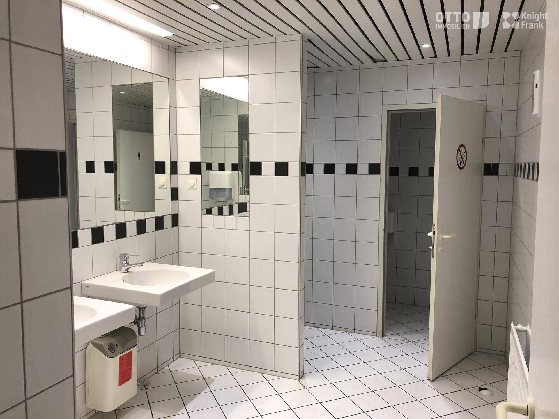 Funktionale Toilettenanlage mit weißen Fliesen, mehreren Waschbecken und Spiegeln, gut gepflegt.