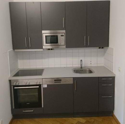 Moderne Küchenzeile mit dunkelgrauen Schränken, integrierten Geräten und weißem Fliesenspiegel.
