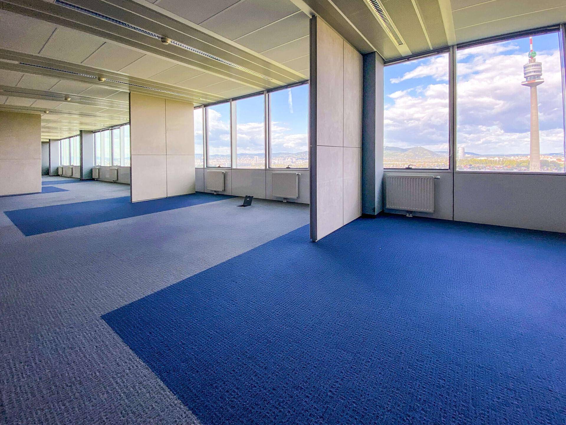 Großzügiger Bürobereich mit farbigem Teppichboden und modularen Trennwänden, bietet einen weiten Blick auf die Stadt.