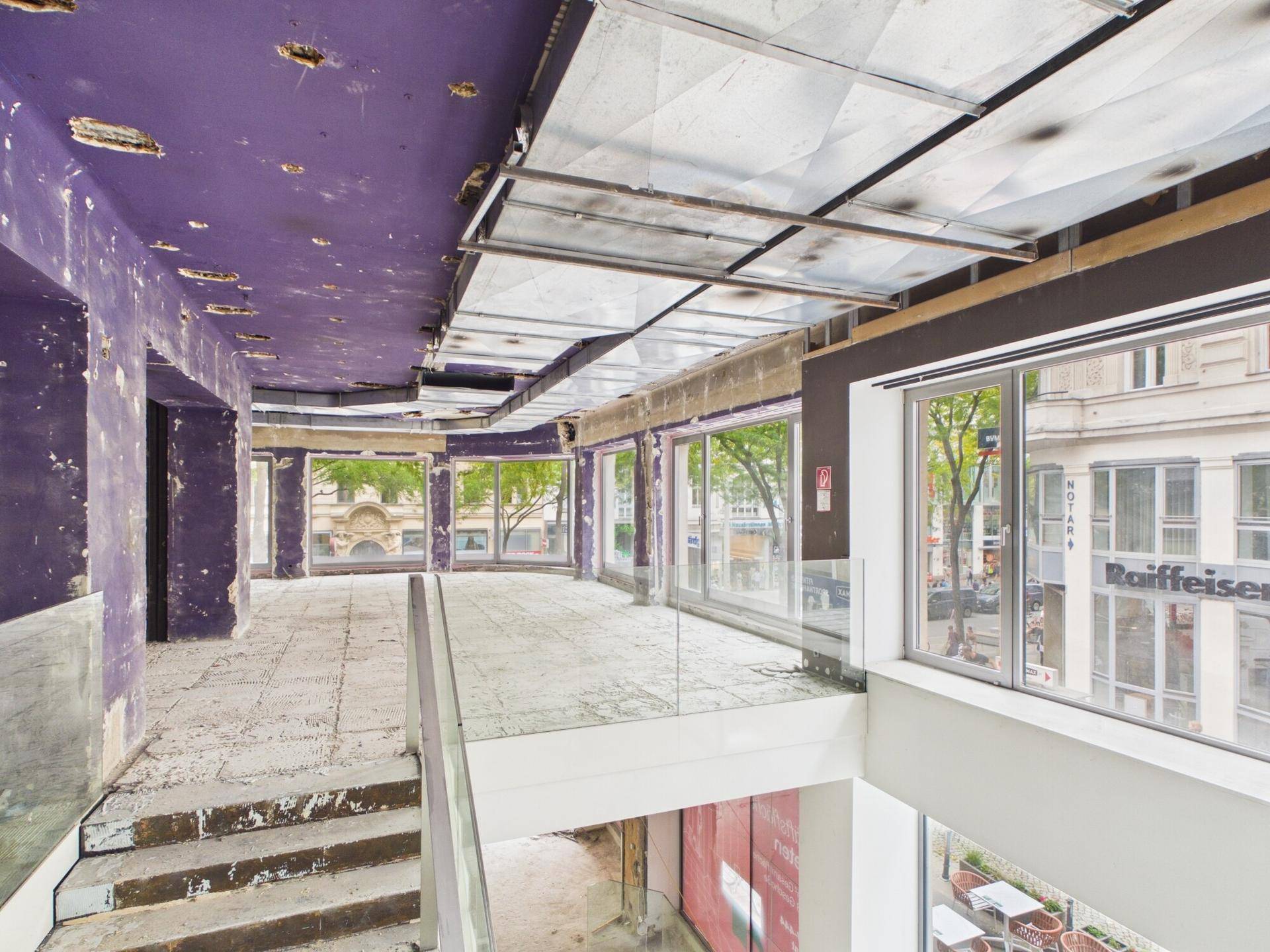 Gewerbefläche im Rohbau mit Zwischengeschoss, Glasgeländer und großen Fenstern mit Stadtblick.