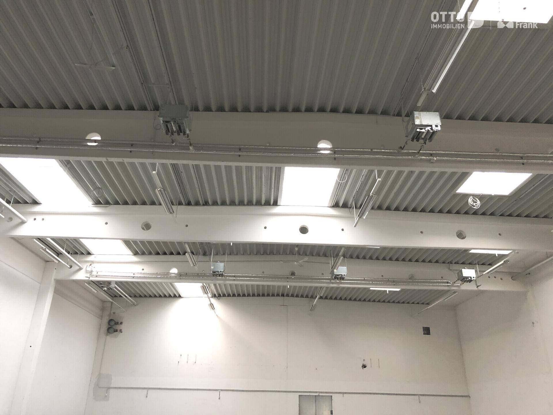 Detailansicht der hohen Deckenkonstruktion mit Oberlichtern und Beleuchtung in der Industriehalle, zeigt offene Träger.