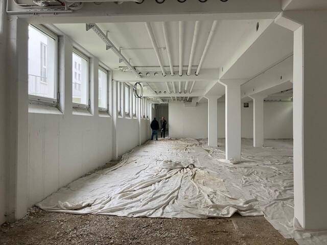 Geräumiger, heller Innenraum mit einer langen Reihe von Fenstern und sichtbaren Deckeninstallationen, bereit zur Umgestaltung.