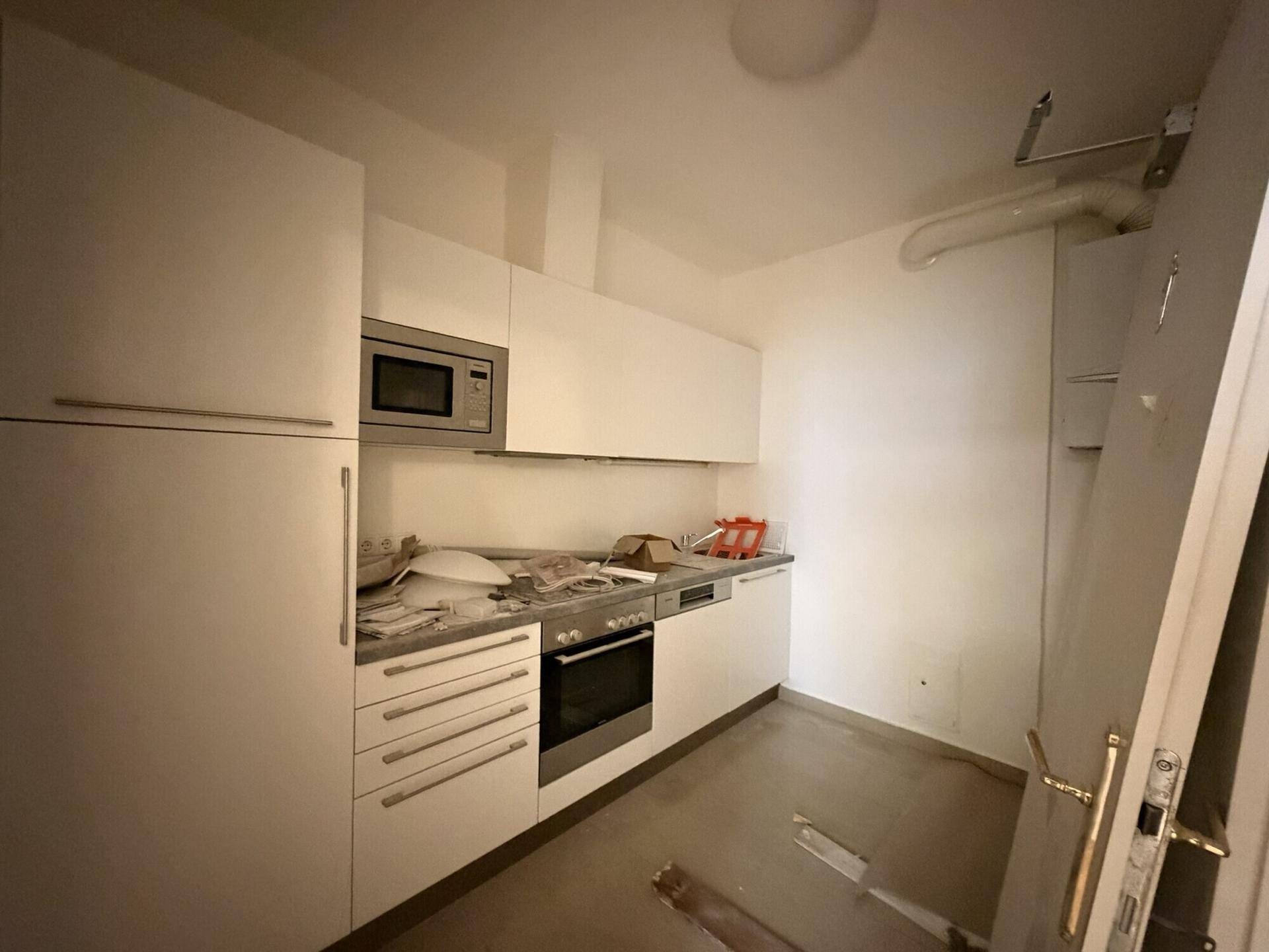 Kompakte Küche mit weißen Schränken, integrierter Mikrowelle und Ofen, bereit zur Fertigstellung.