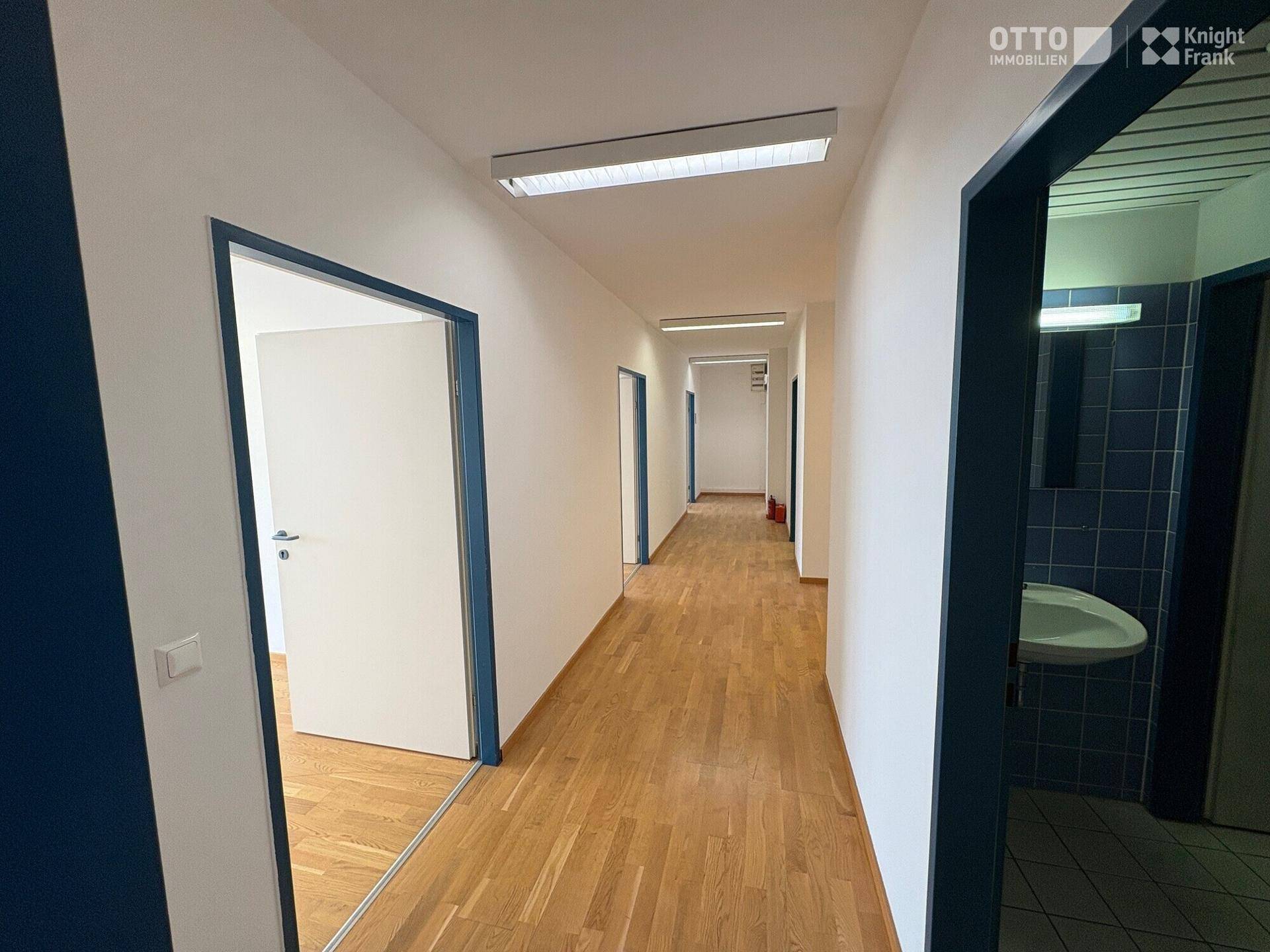 Langer, heller Flur mit Holzfußboden und mehreren Türen, die zu Büroräumen führen.