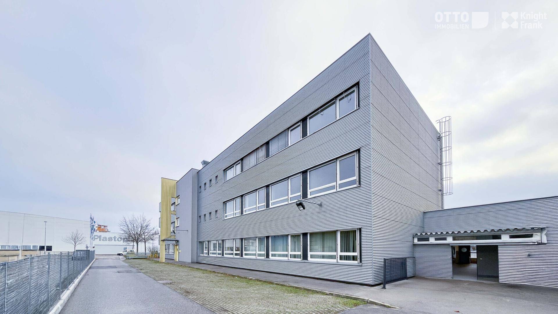 Modernes Bürogebäude mit geriffelter Metallfassade und großen Fenstern unter bewölktem Himmel.
