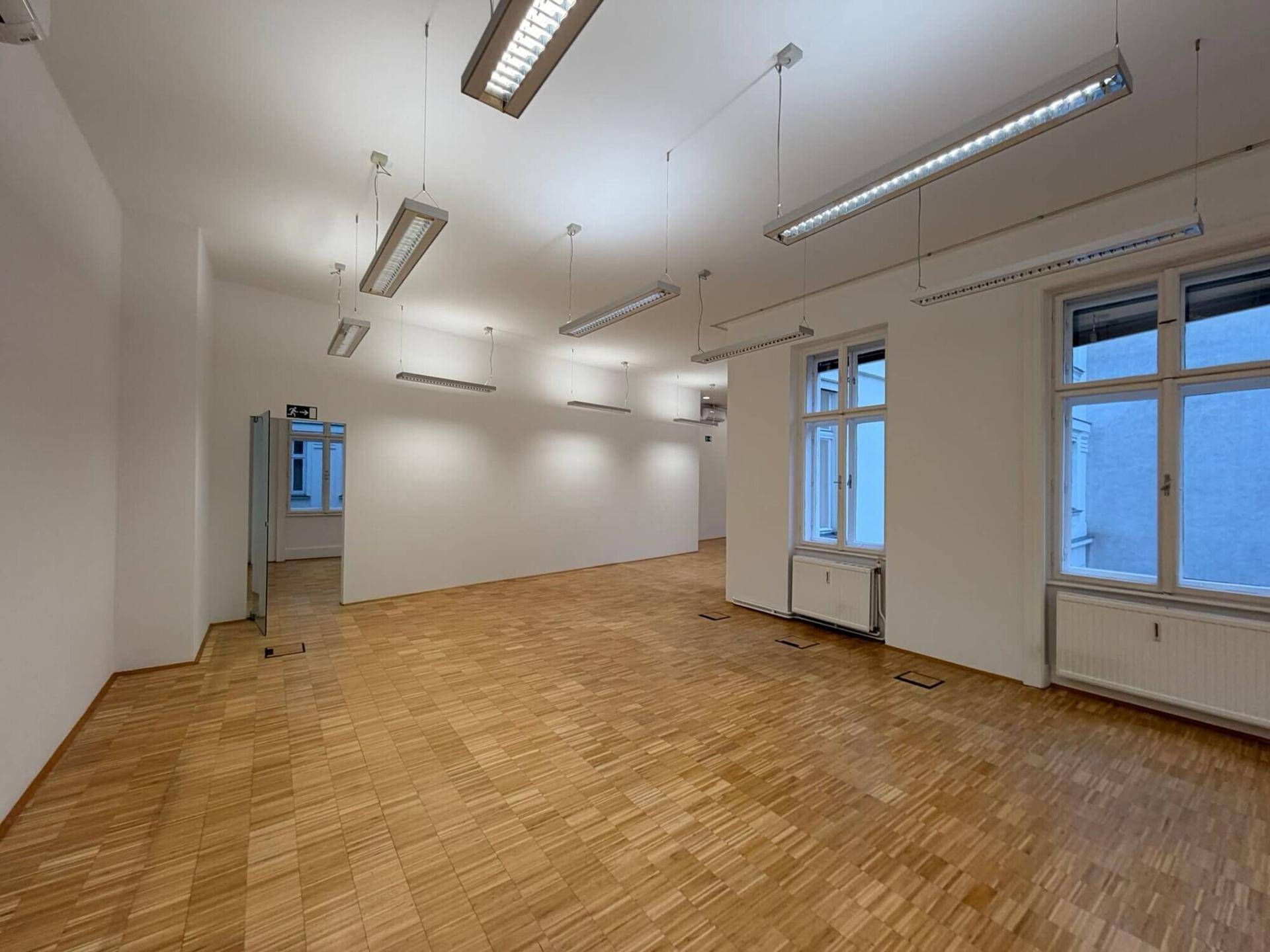 Großer, leerer Büroraum mit hellem Parkettboden, hohen Decken und zahlreichen Fenstern, bereit für die individuelle Einrichtung.
