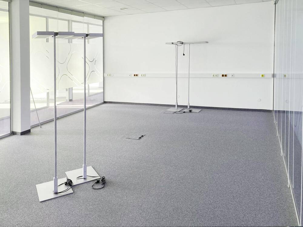 Großer, heller Büroraum mit Teppichboden, Glaswänden und viel Tageslicht.
