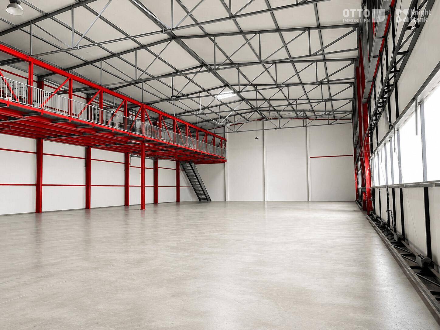 Weitläufige Industriehalle mit roter Stahlkonstruktion, hoher Decke und einem Zwischengeschoss.