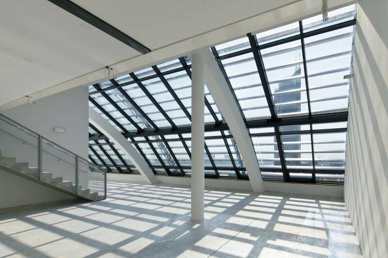 Heller Treppenbereich mit großen Glasfenstern und einem schrägen Glasdach, das interessante Lichtmuster erzeugt.