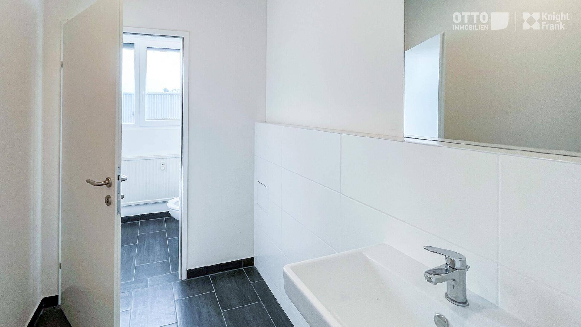 Modernes Badezimmer mit dunklen Fliesen und weißem Waschbecken, sauber und funktional.