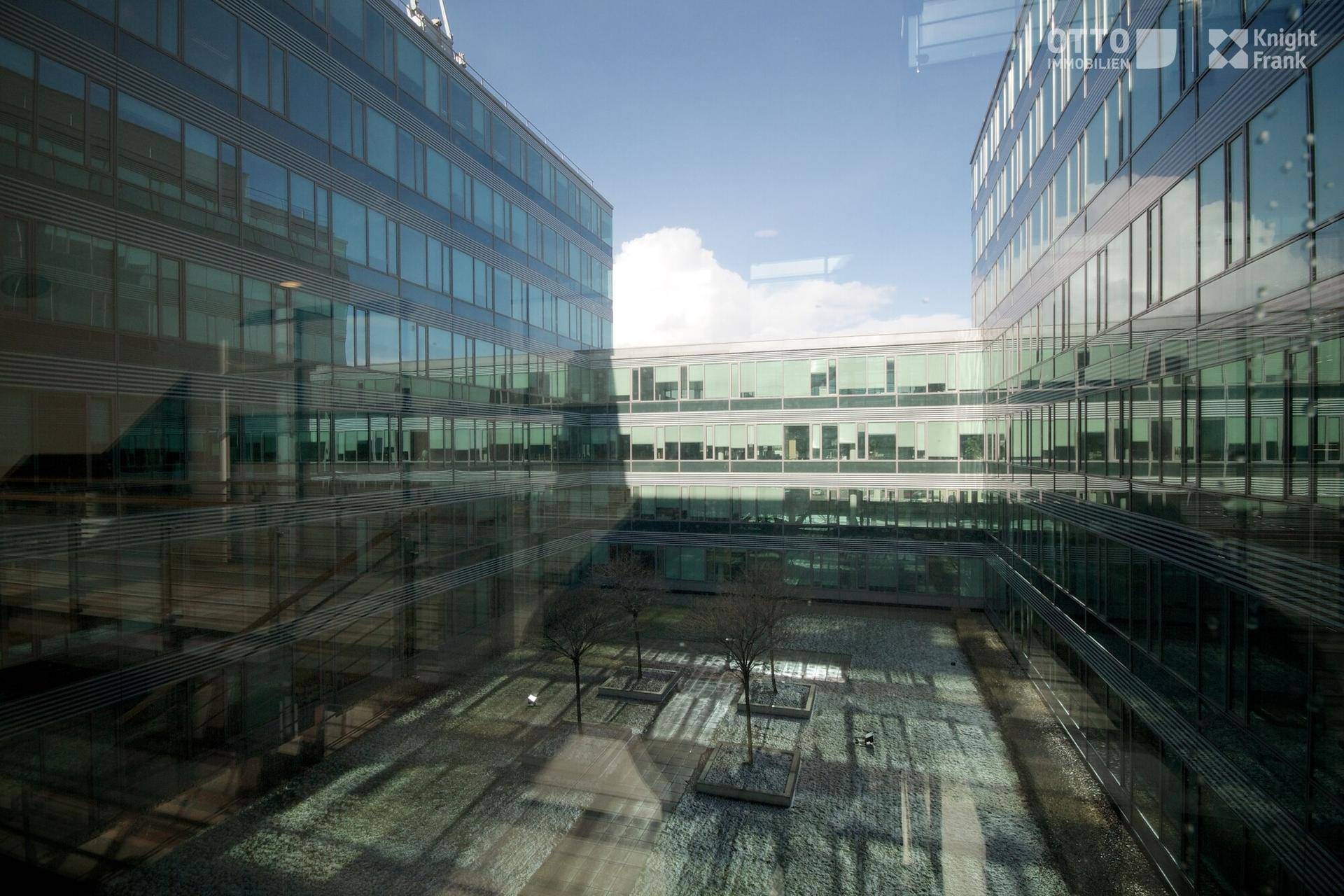 Innenhofansicht eines modernen Bürokomplexes mit reflektierenden Glasfassaden und einem begrünten Bereich.