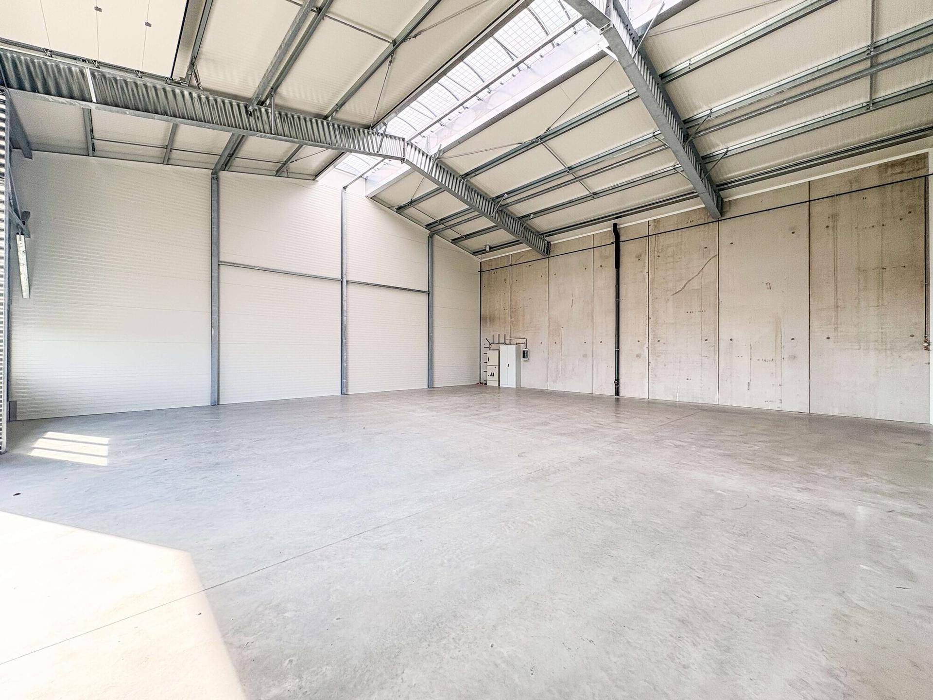 Weitläufige, ungenutzte Lagerhalle mit hohen Decken, Betonwänden und Oberlichtern für helle Arbeitsbereiche.