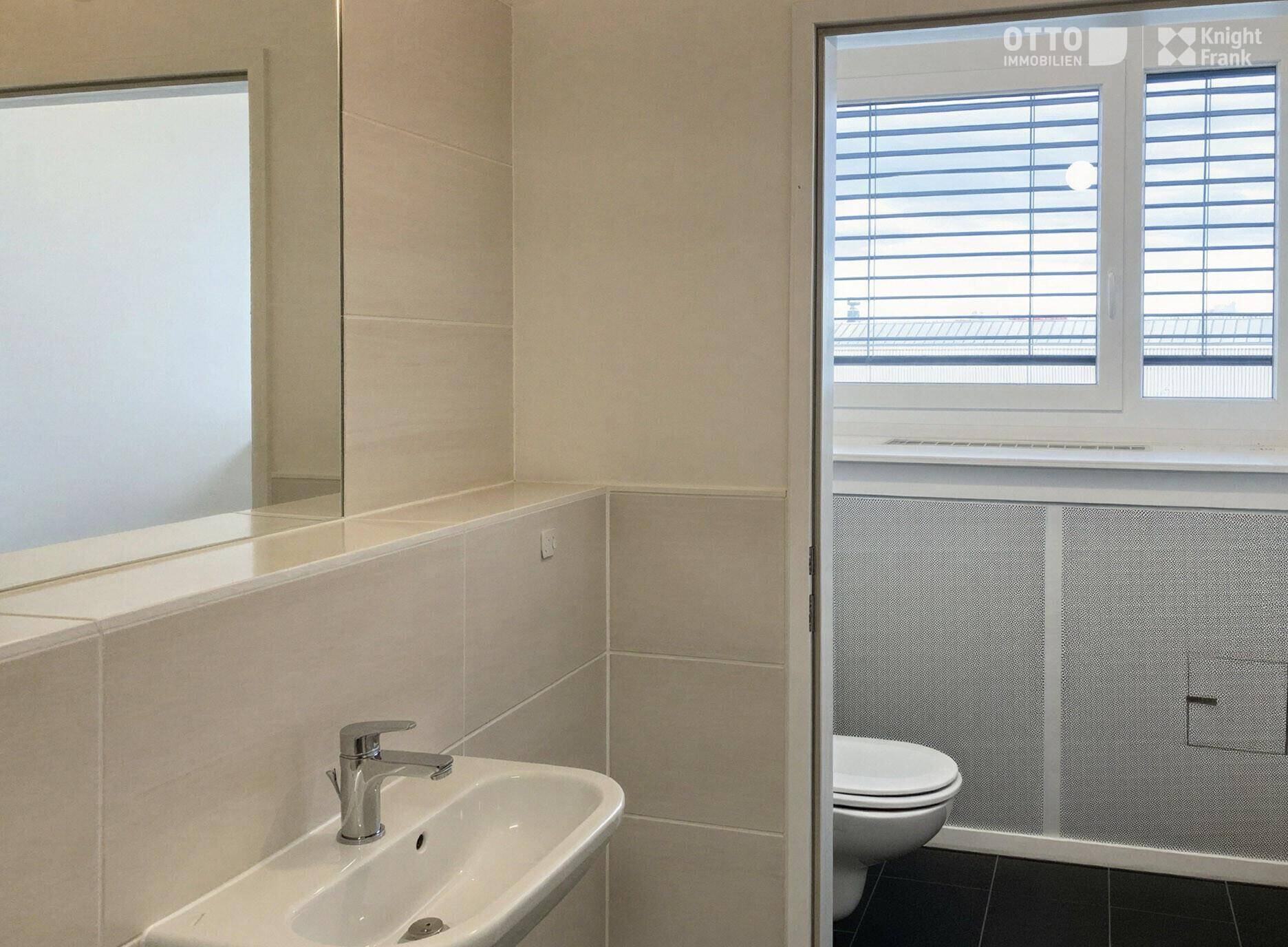 Modernes WC mit Wandfliesen, Waschbecken und Fenster mit Jalousien für Privatsphäre.