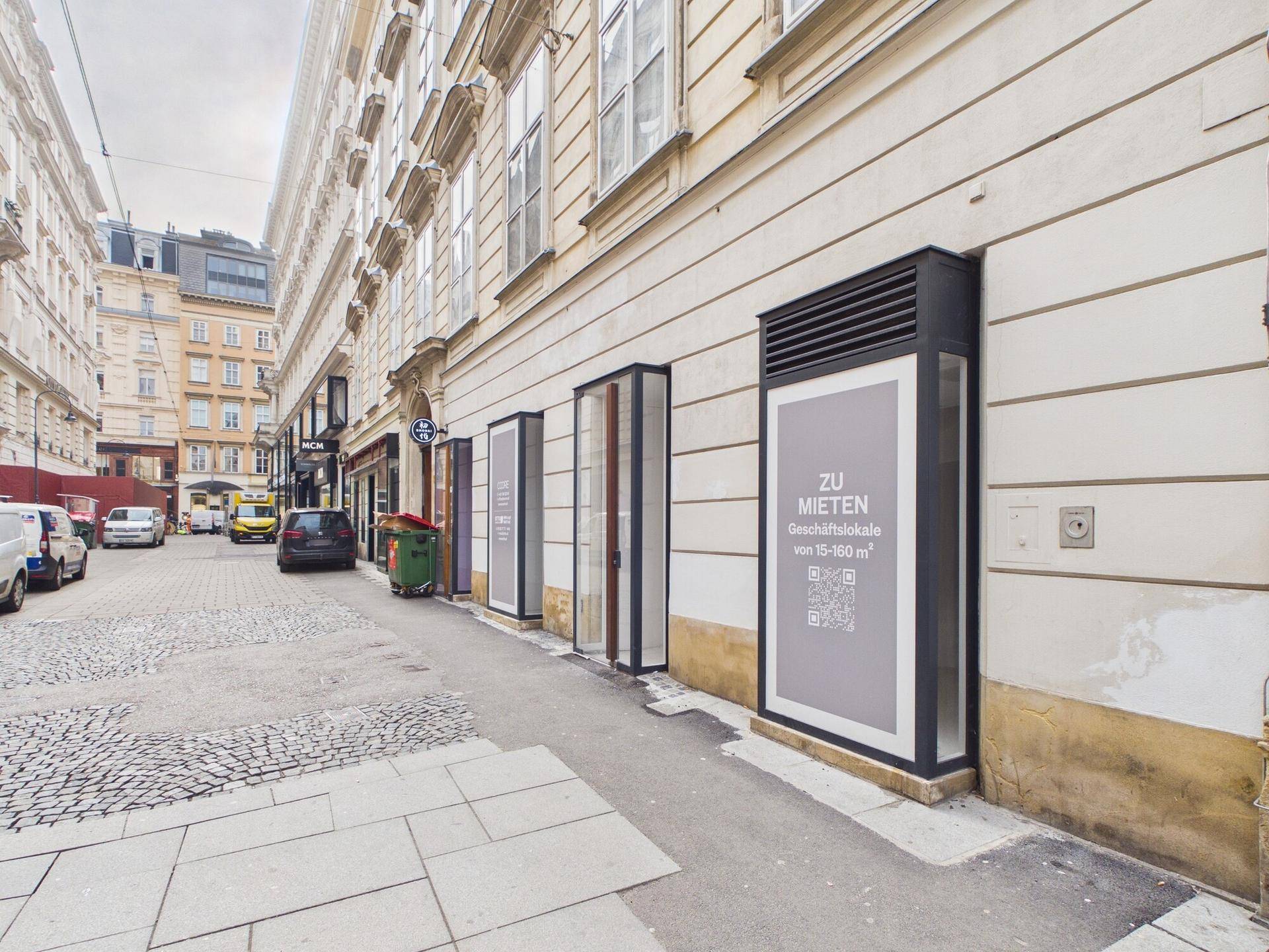 Straßenansicht der Geschäftsfassade mit umliegenden Gebäuden und parkenden Fahrzeugen in einer städtischen Umgebung.