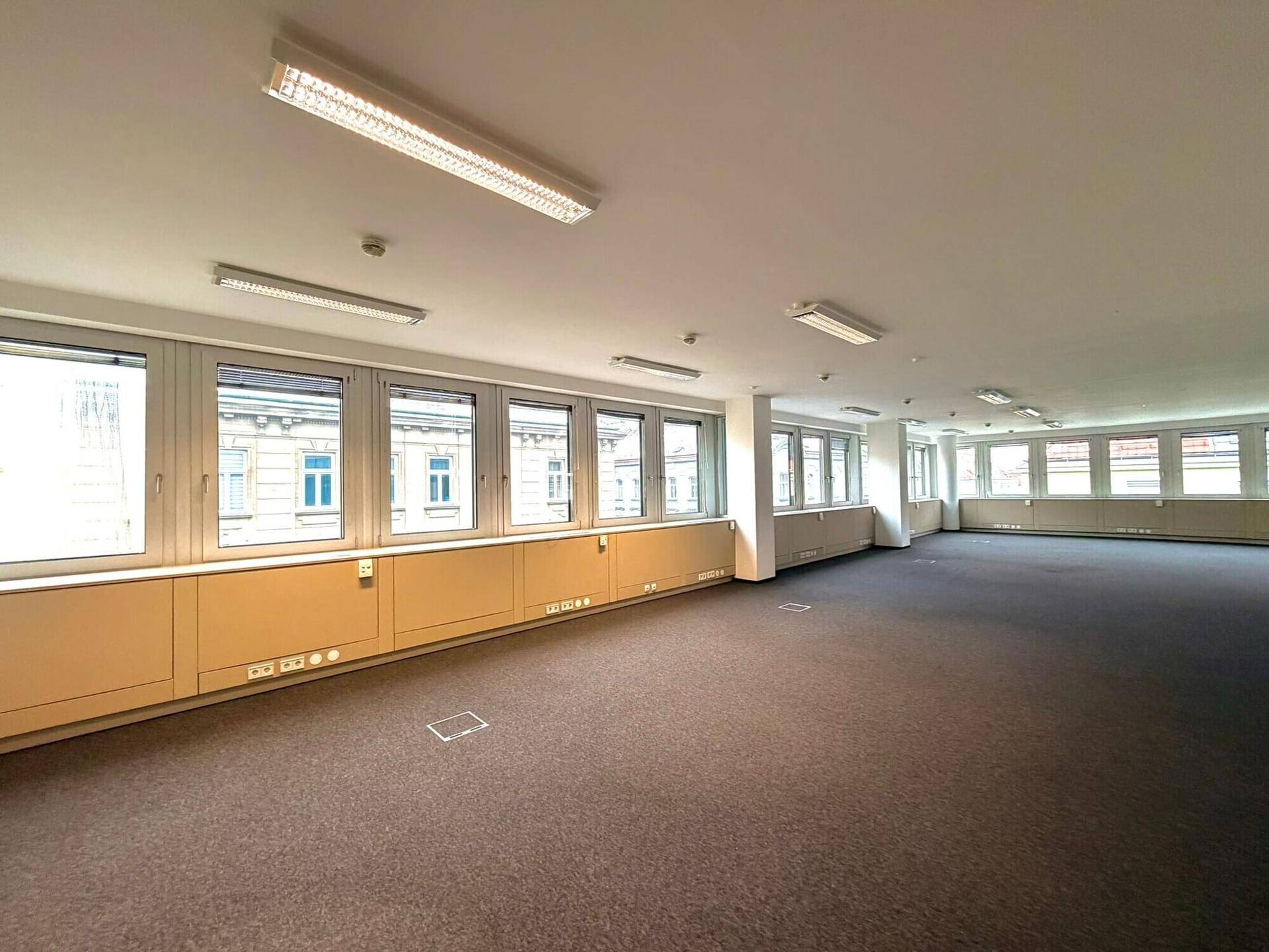 Weitläufiger Bürobereich mit durchgehender Fensterfront, Teppichboden und guter Beleuchtung.