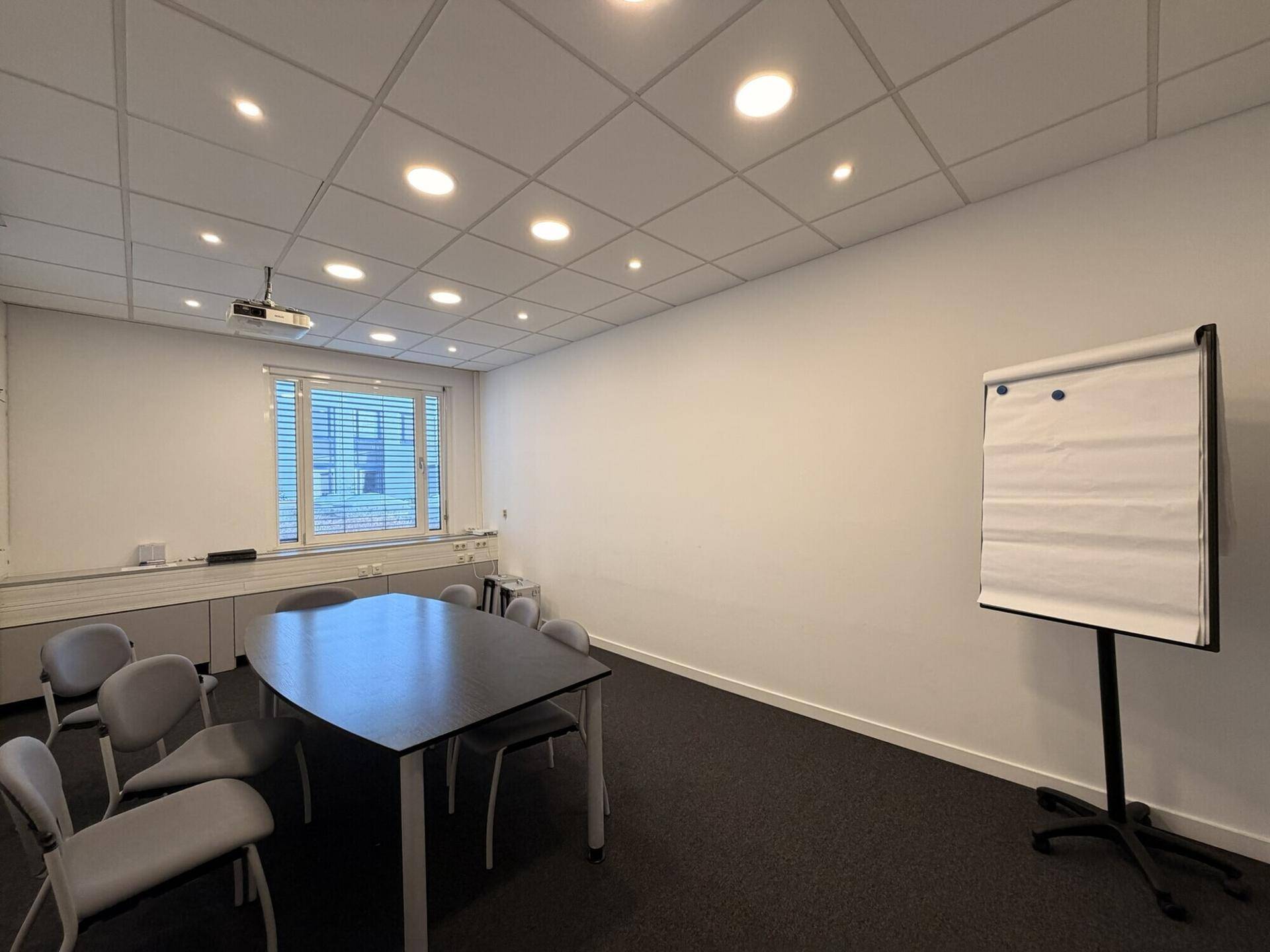Geräumiger Konferenzraum mit Flipchart, großem Tisch und Beamer, bereit für Präsentationen.