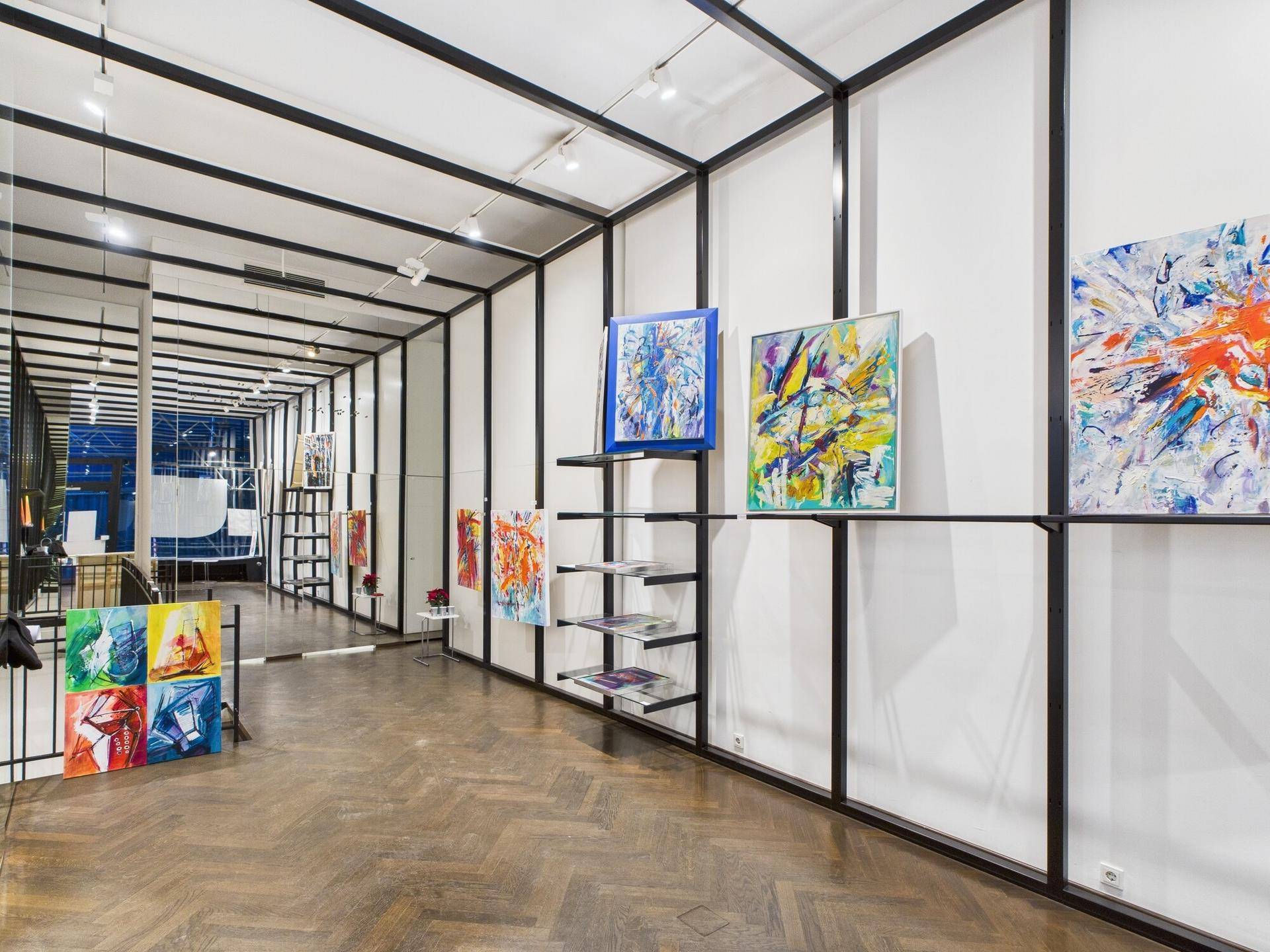Heller und moderner Galerieraum mit Fischgrätparkett, schwarzen Metallrahmen und abstrakten Kunstwerken.