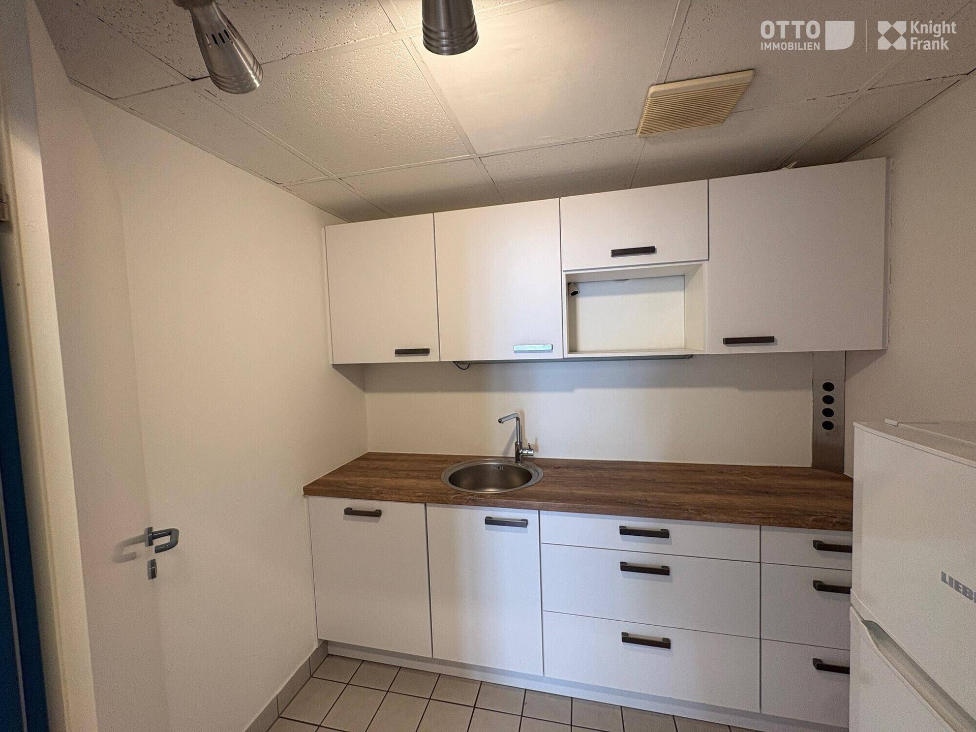 Kleine Küchenzeile mit weißen Schränken, Holztheke und Spülbecken in einem funktionalen Raum.