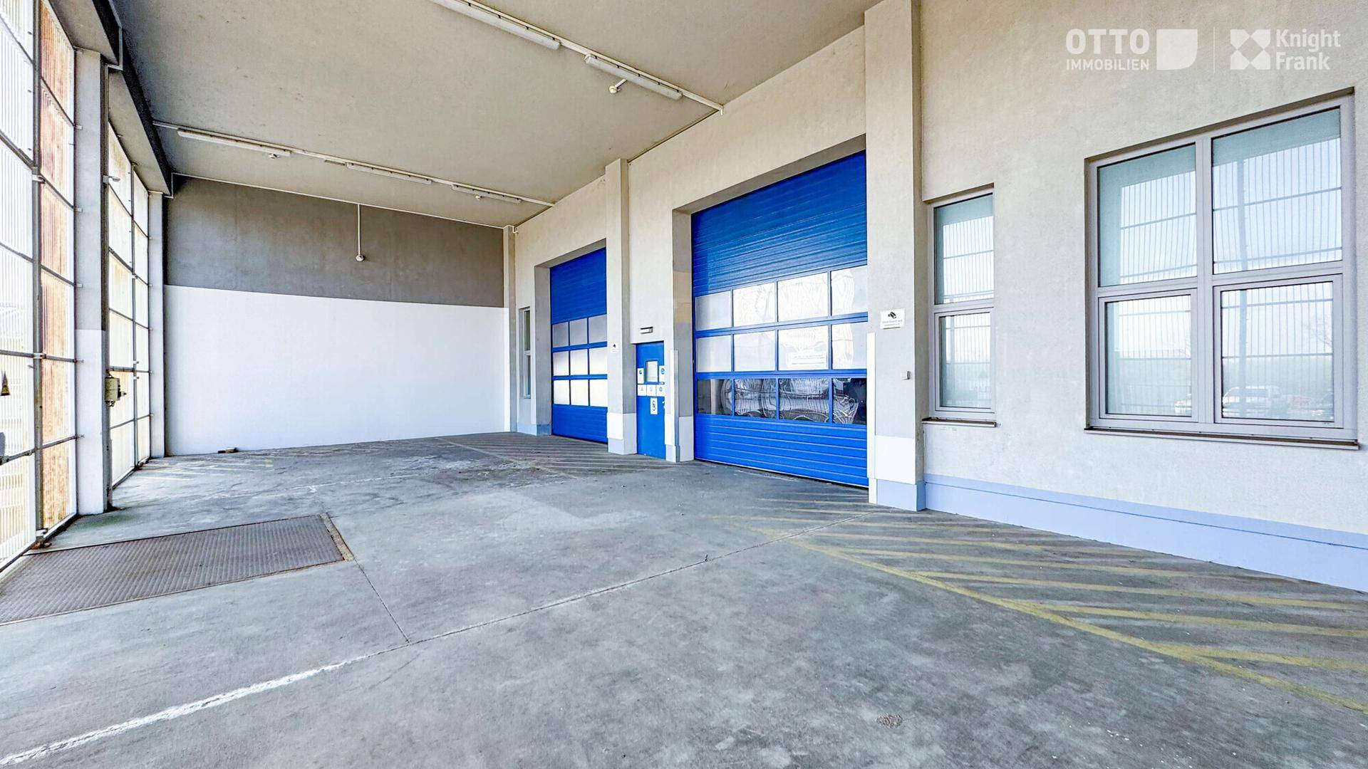 Geräumige Lagerhalle mit robustem Betonboden und zwei großen blauen Rolltoren für den Zugang.