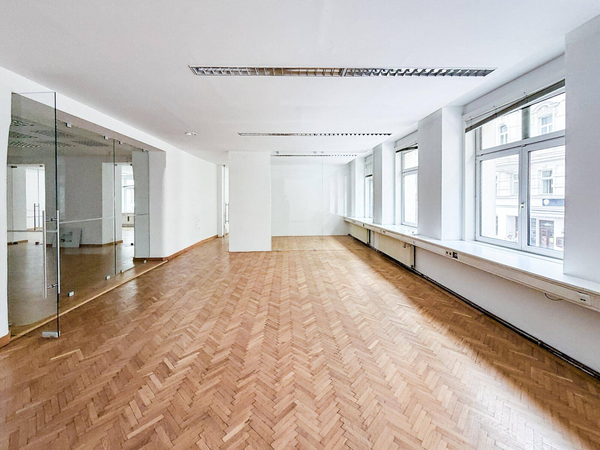 Heller und geräumiger Büroraum mit Fischgrätparkett und großen Fenstern, ideal für flexible Arbeitsplatzgestaltung.