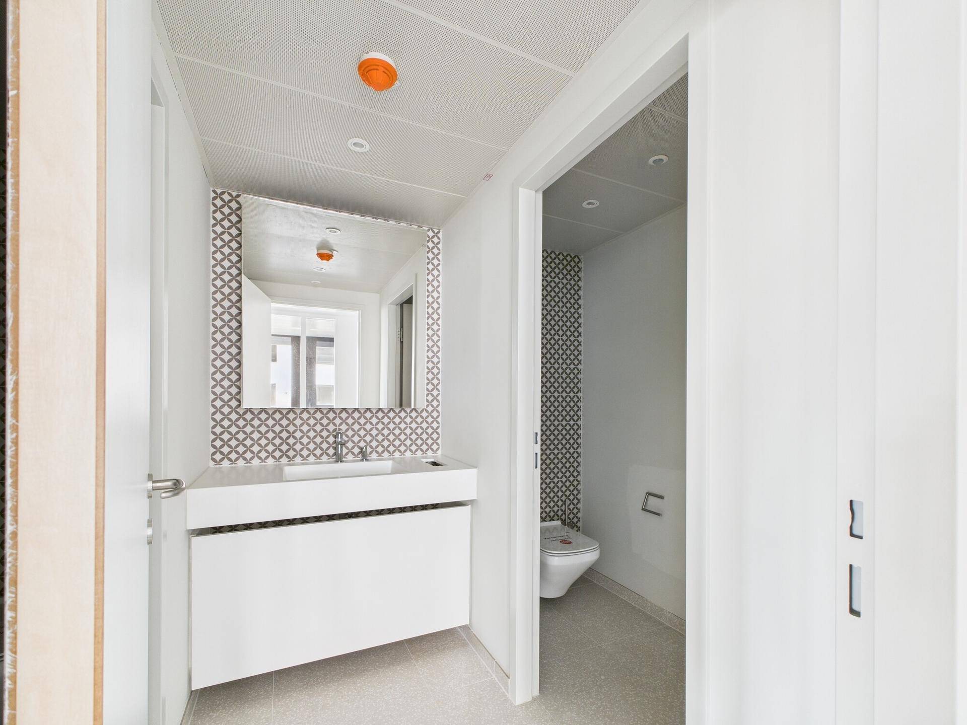 Modernes Badezimmer mit Waschbecken, Spiegel und WC, ausgestattet mit stilvollen gemusterten Fliesen.