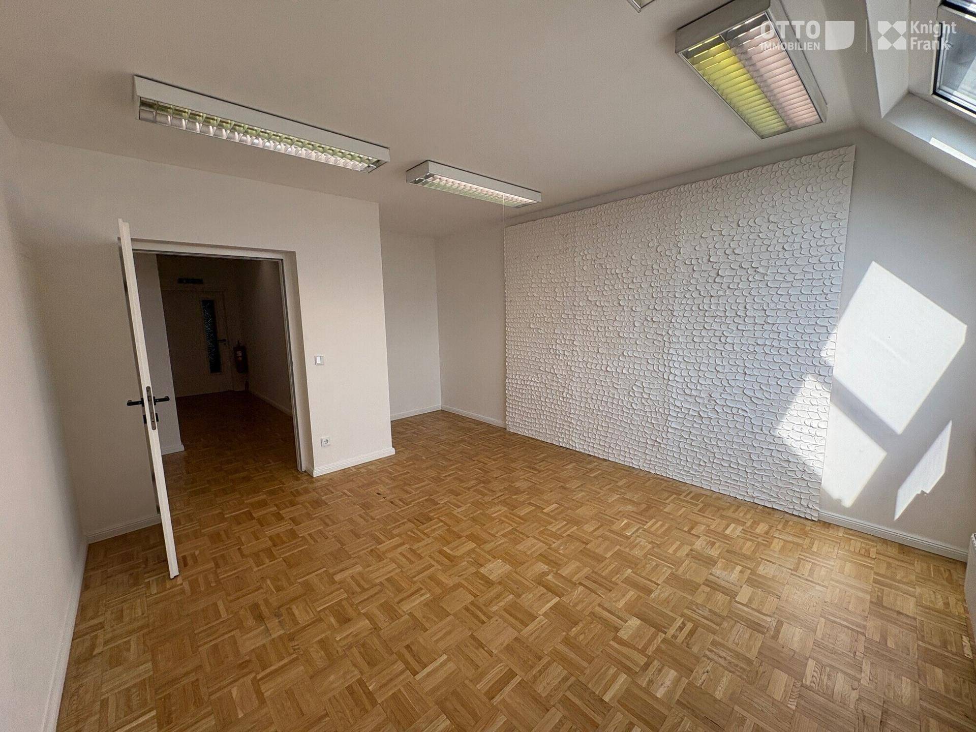 Heller Büroraum mit Parkettboden und einer strukturierten Wand, bereit zur individuellen Gestaltung.